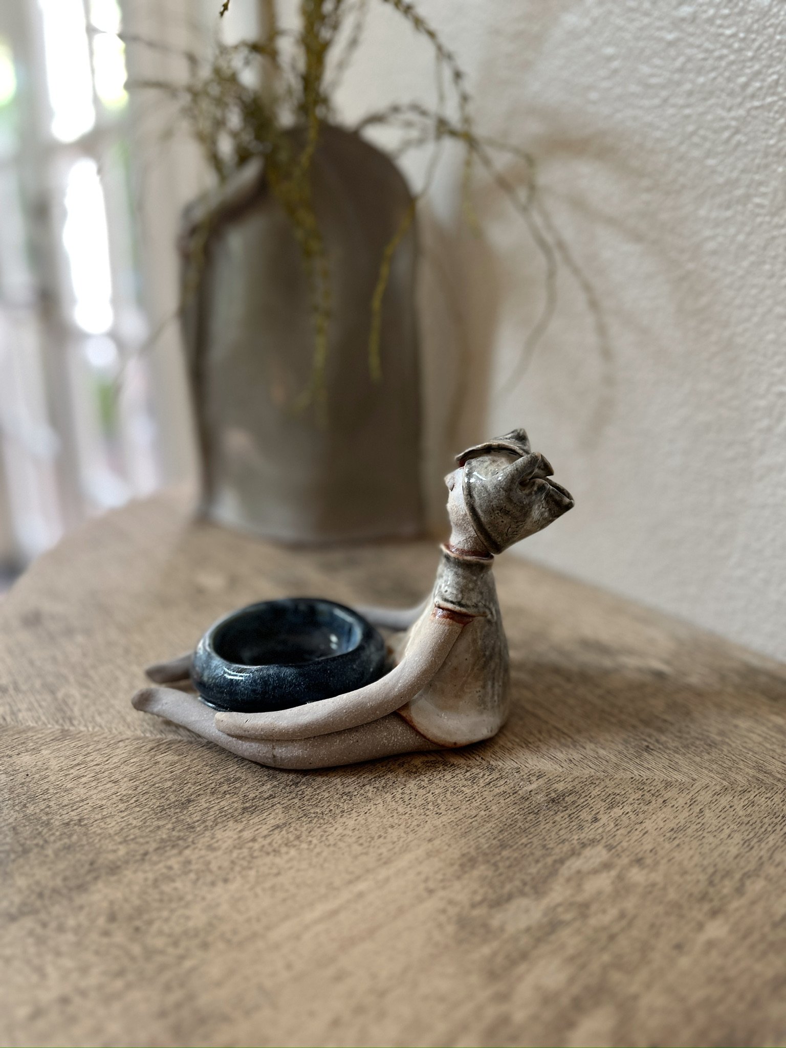 Glazed and Fired ceramic handmade sculpture of a lady holding a blue bowl and sitting on a table. Image from the left.