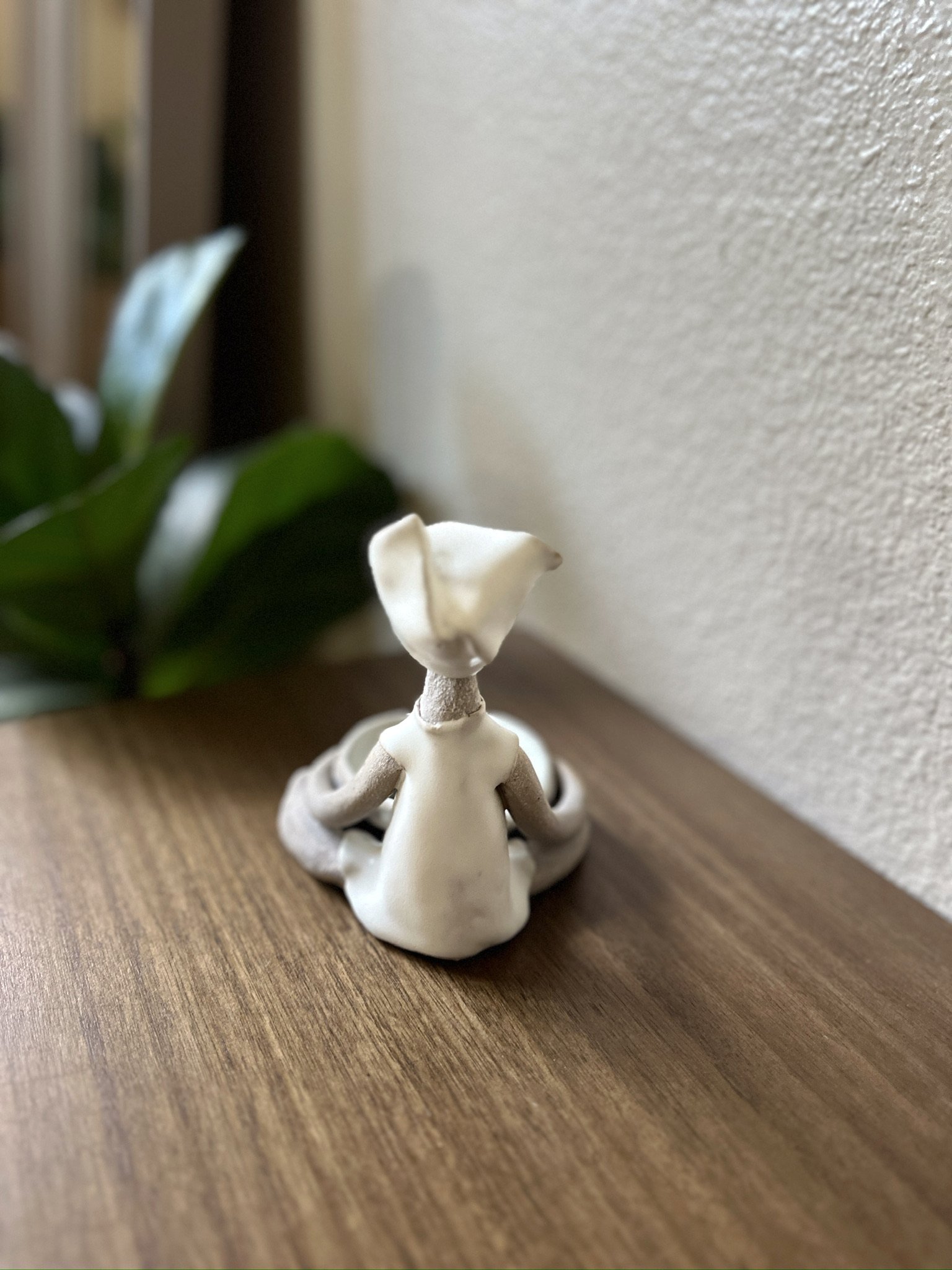 Glazed and Fired ceramic handmade sculpture of a lady holding a multi-colored bowl and sitting on a table. Image from the back.