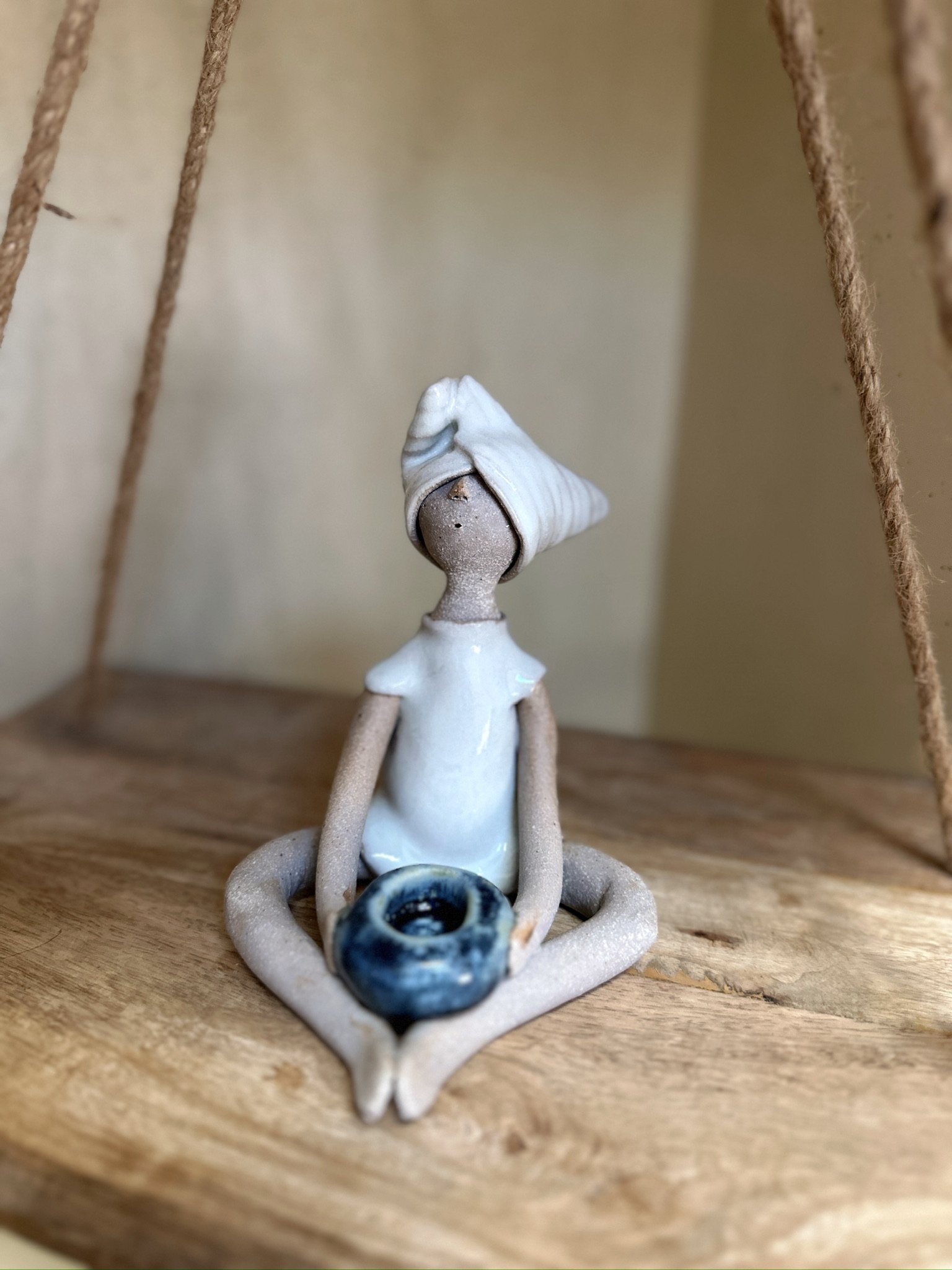 Glazed and Fired ceramic handmade sculpture of a lady sitting with a blue candle holder in her hands. Image from the front.