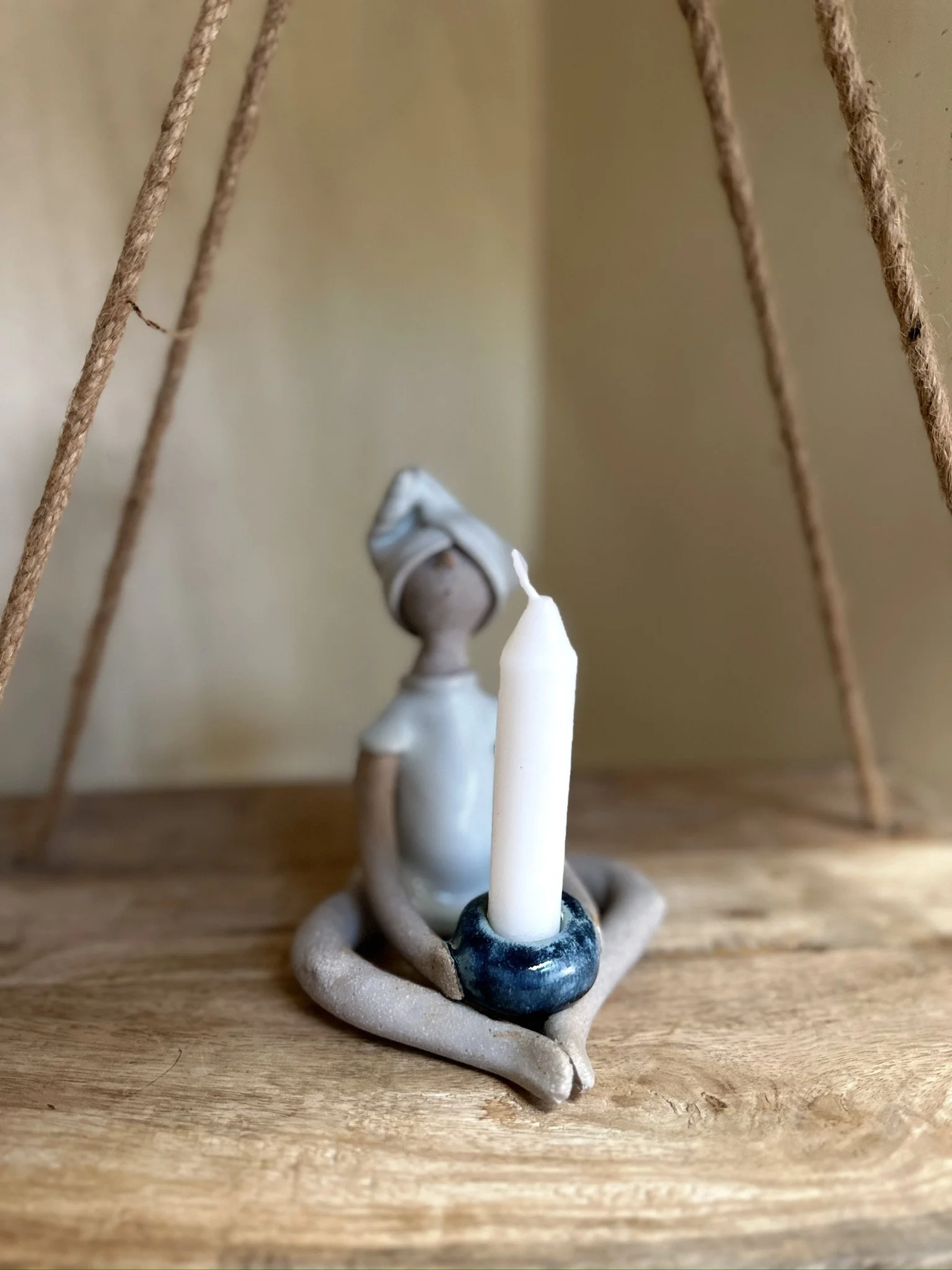 Glazed and Fired ceramic handmade sculpture of a lady sitting with a blue candle holder in her hands. Image from the front with candle.