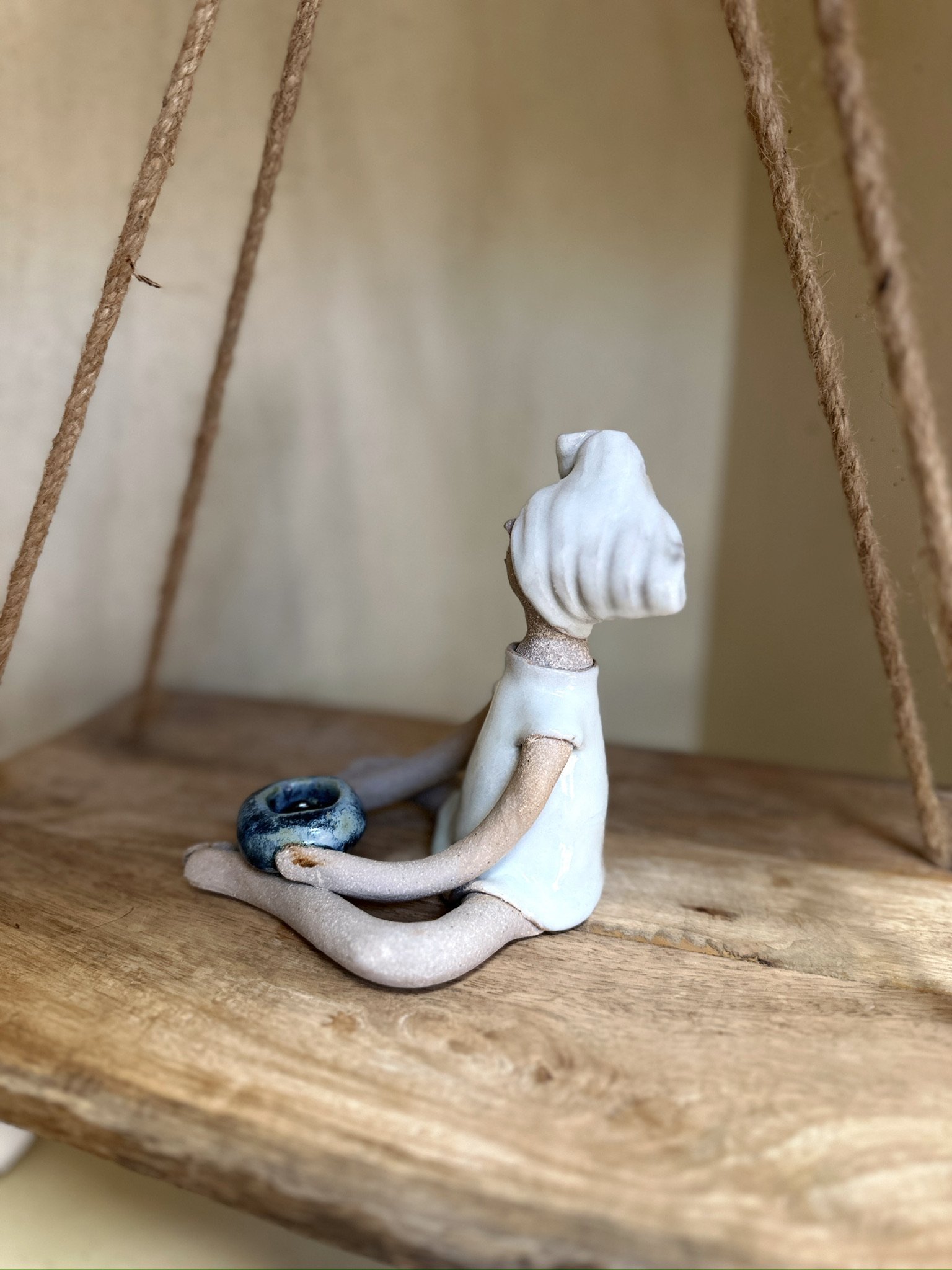 Glazed and Fired ceramic handmade sculpture of a lady sitting with a blue candle holder in her hands. Image from the left.