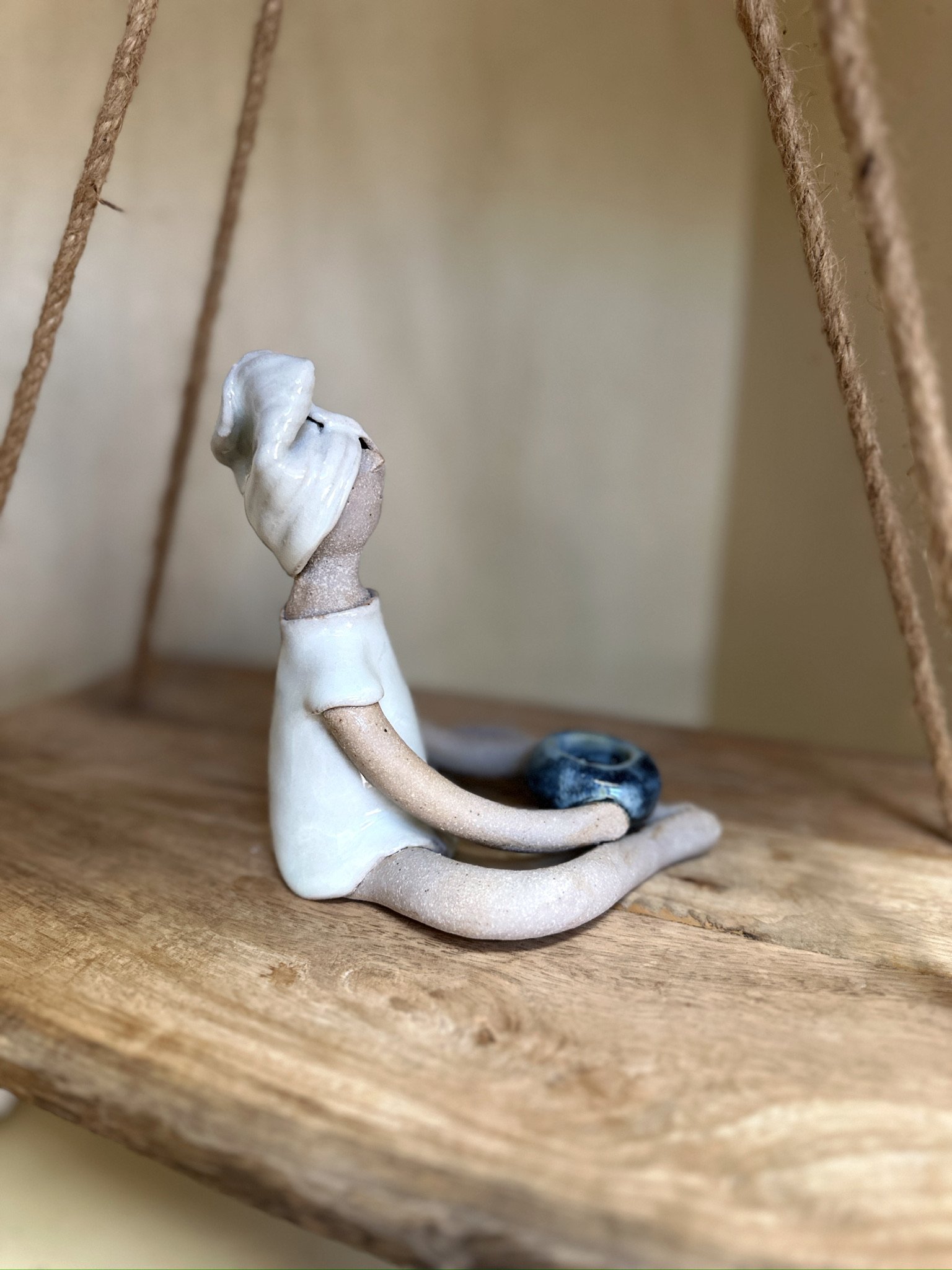 Glazed and Fired ceramic handmade sculpture of a lady sitting with a blue candle holder in her hands. Image from the right.