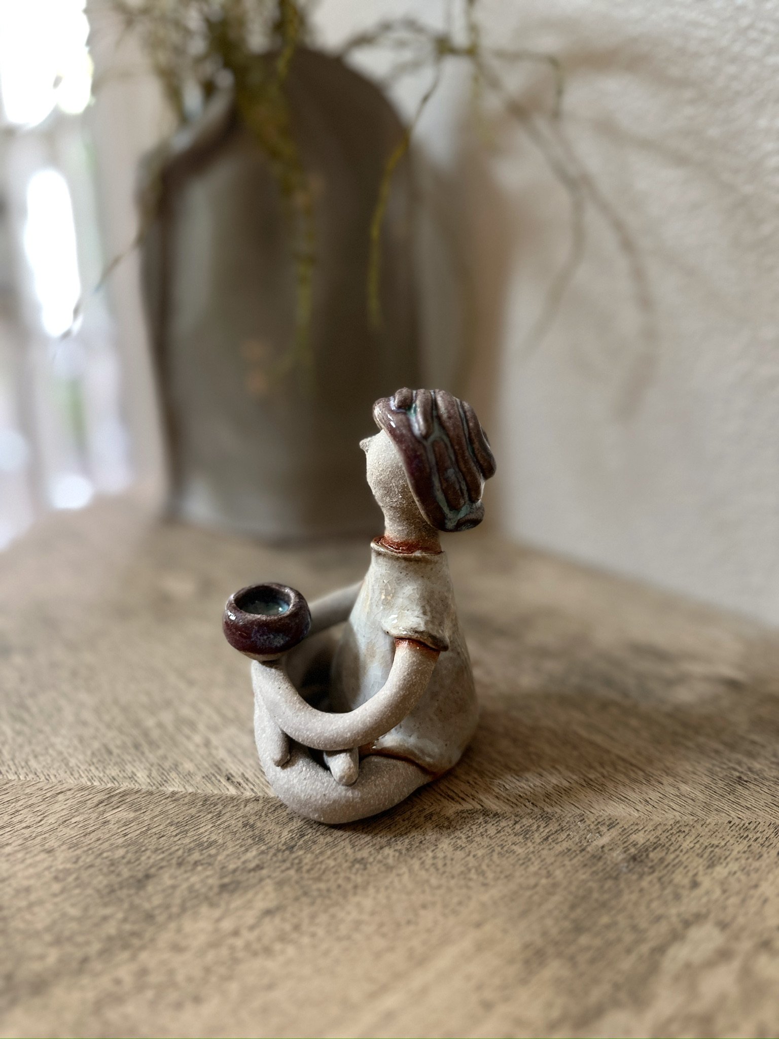 Glazed and Fired ceramic handmade sculpture of a lady holding an incense holder and sitting on cross-legged. Image from the left.