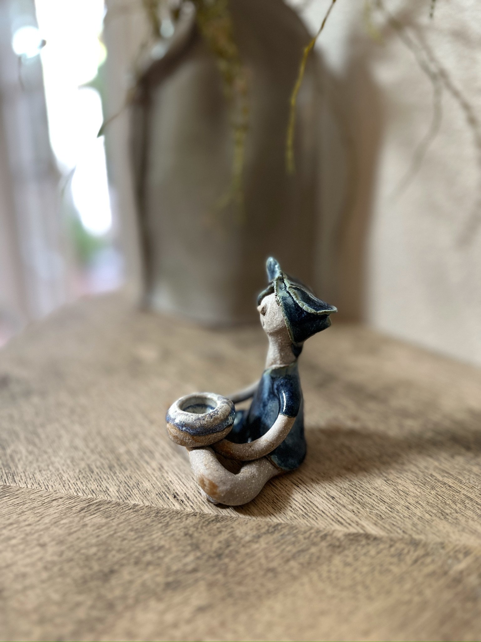 Glazed and Fired ceramic handmade sculpture of a lady with an incense holder and sitting cross-legged on a table. Image from the left.