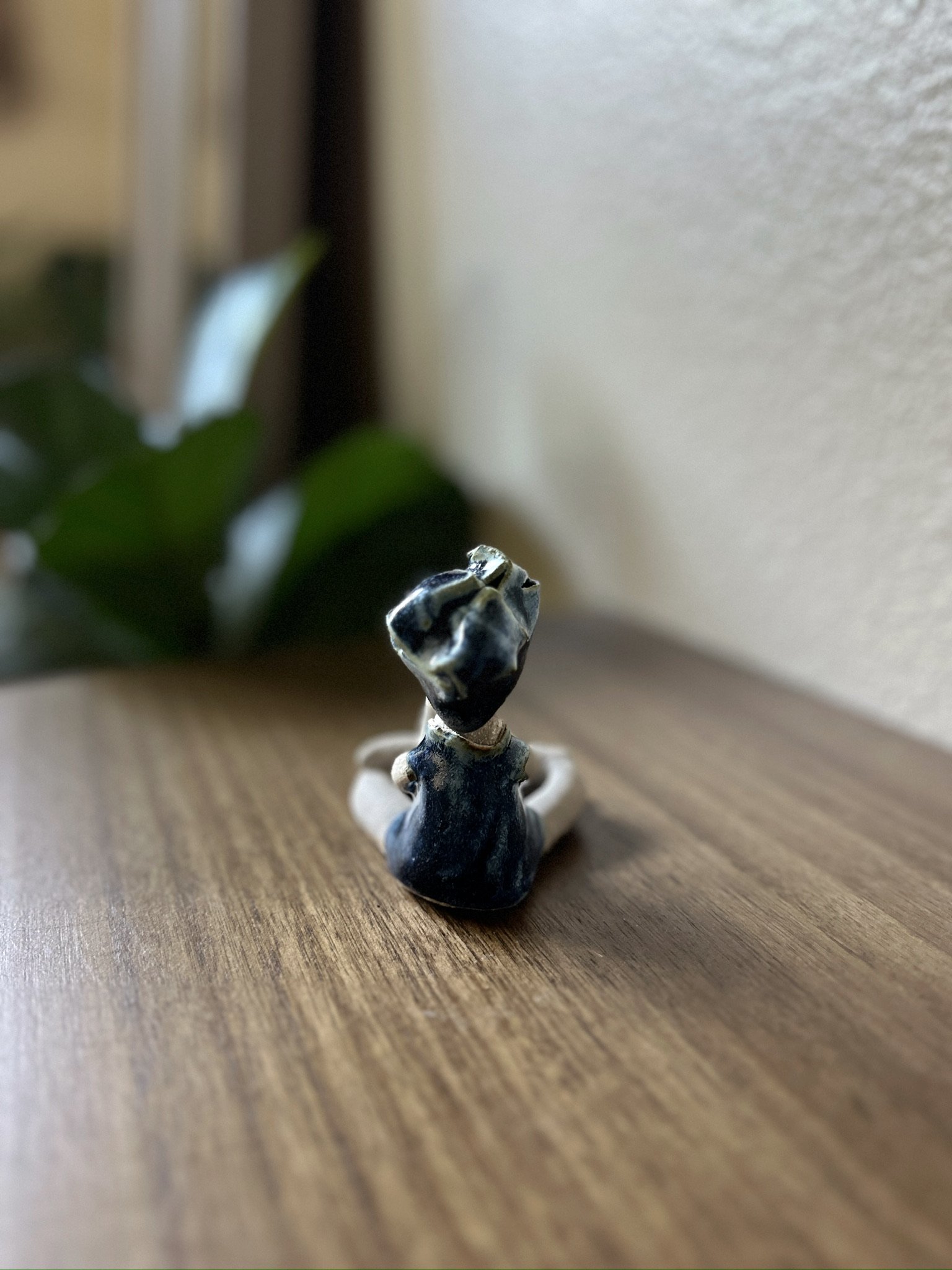 Glazed and Fired ceramic handmade sculpture of a lady with her hands in prayer position and sitting cross-legged on a table. Image from the back.