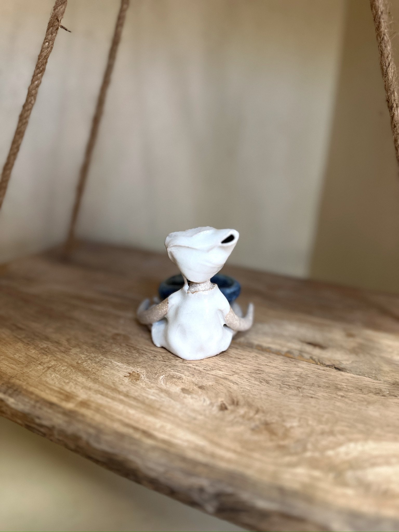 Glazed and Fired ceramic handmade sculpture of a lady with a small blue bowl and sitting on a swing. Image from the back.