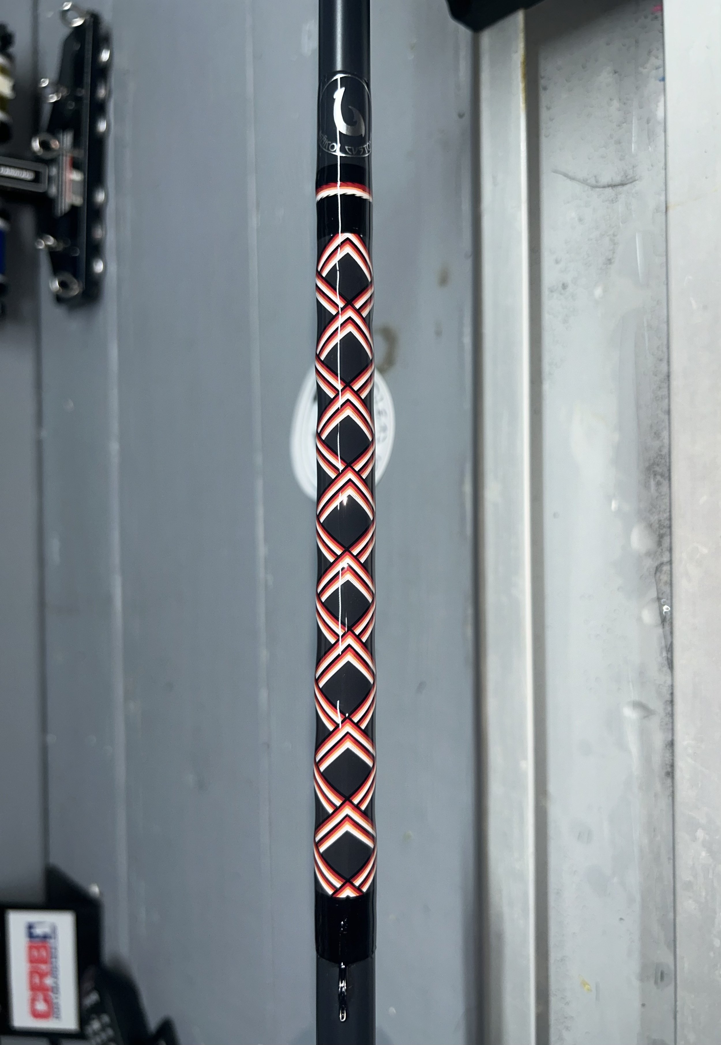 Intricately wrapped fishing rod with black, red, and white diamond pattern on a grey background.