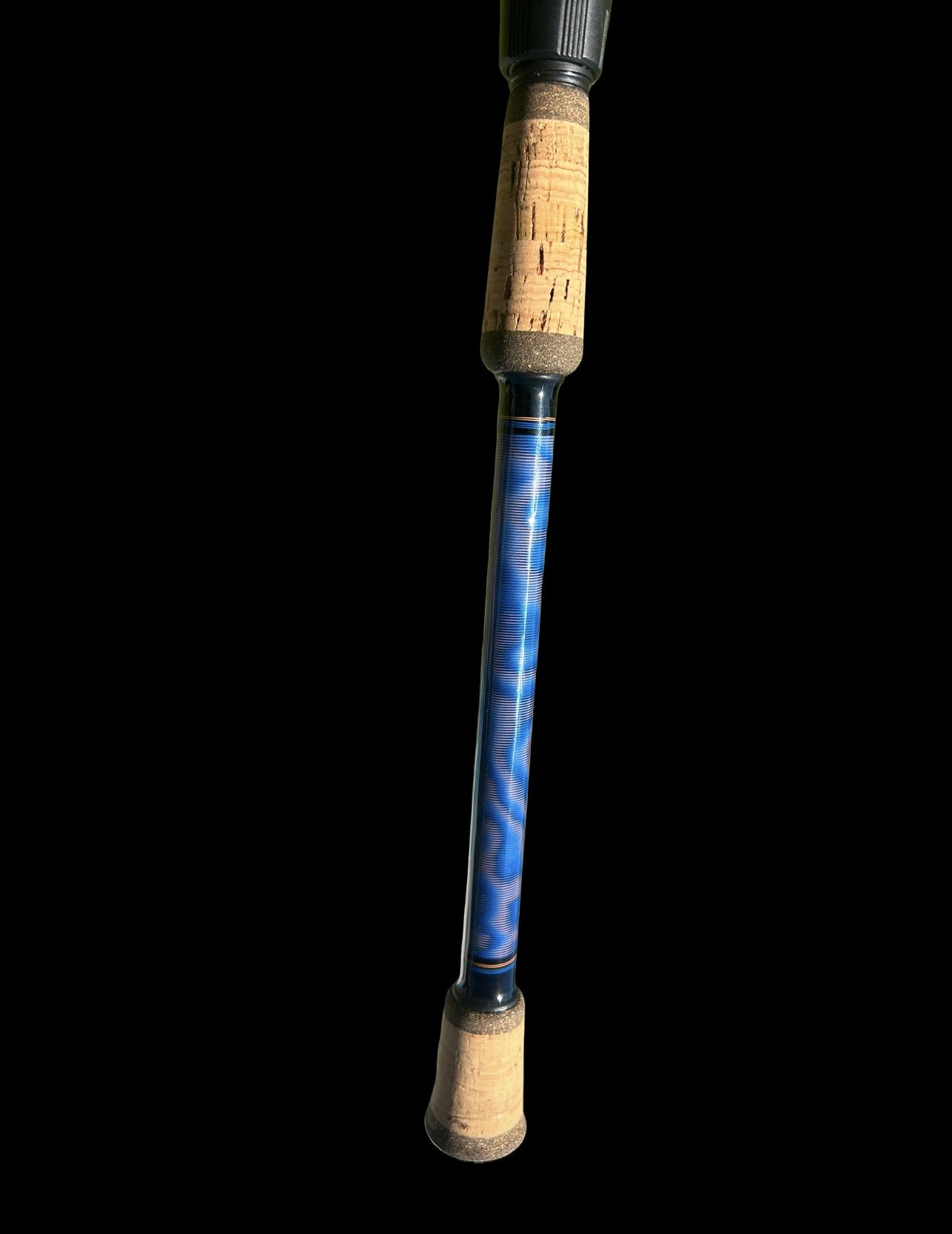 Close-up of a fishing rod handle with cork grip and blue patterned shaft on a black background.