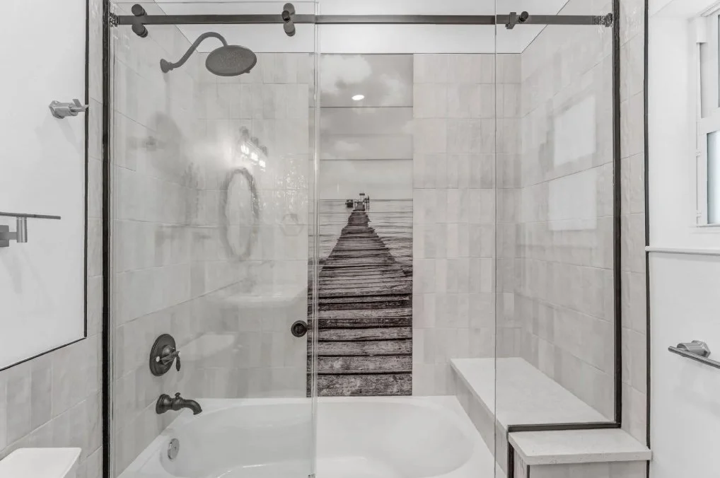 Bathroom with a glass shower enclosure, a rain showerhead, a built-in bench, and a wall art of a pier leading to the ocean.