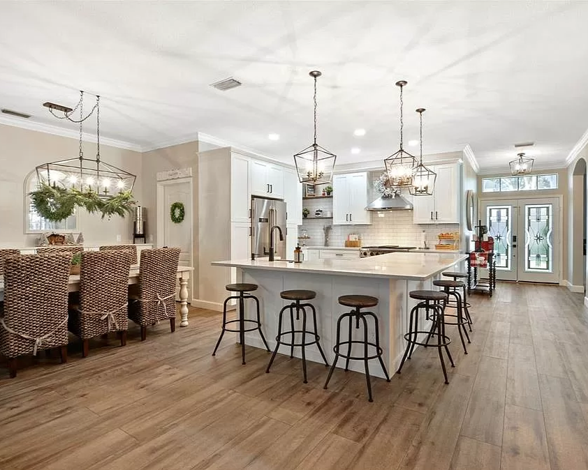 Open-concept kitchen and dining area with white cabinetry, island, bar stools, and woven dining chairs, decorated with Christmas greenery and modern light fixtures.