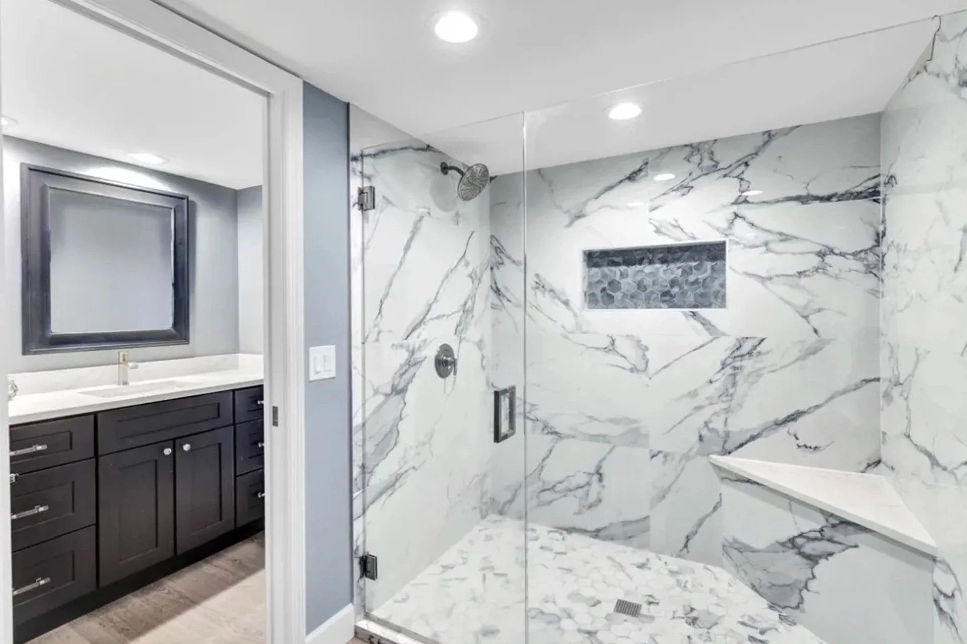 Modern bathroom with marble shower, glass door, and dark vanity with white countertop