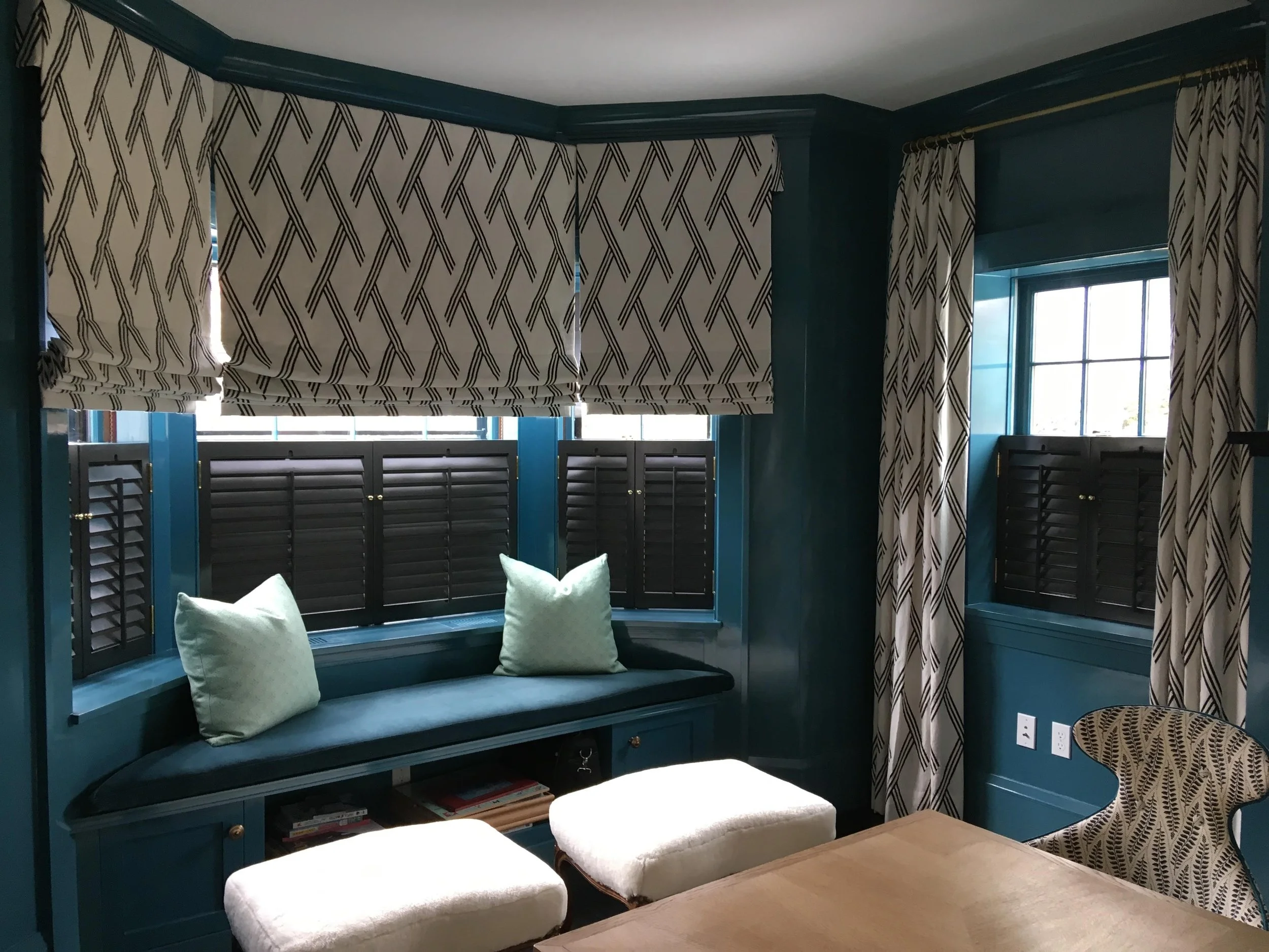 Room with teal walls, patterned curtains, a bay window seat with mint cushions, and upholstered furniture.