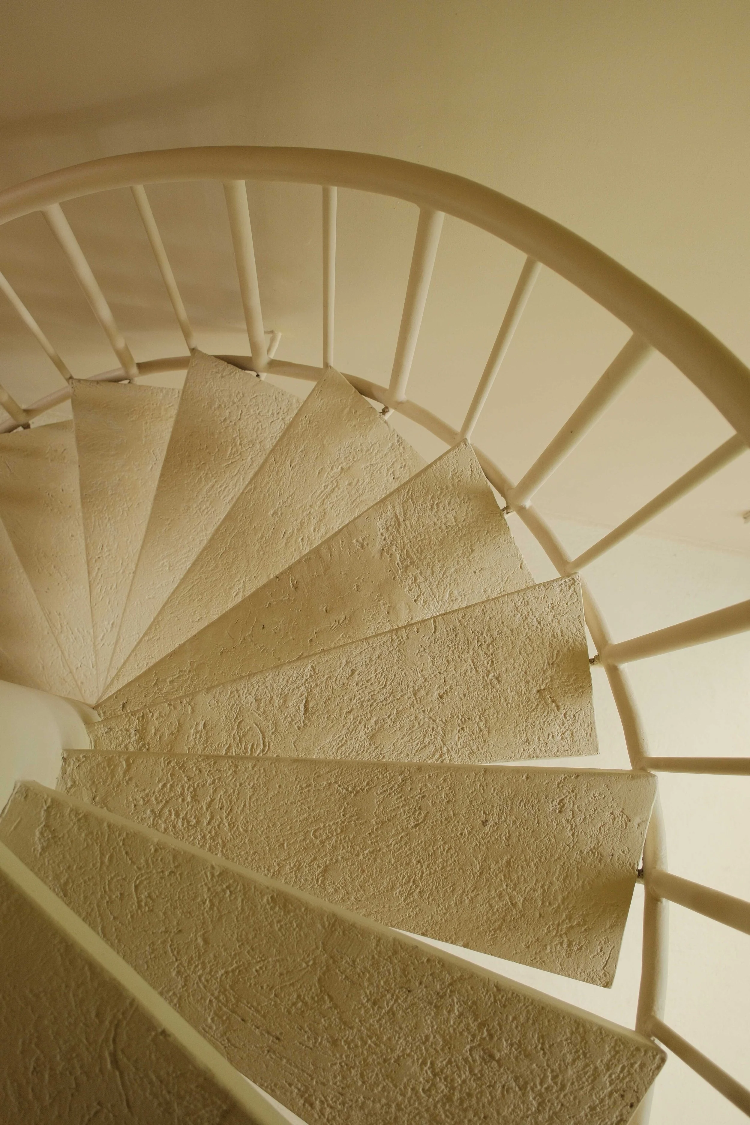 Curved spiral staircase with textured beige steps and white metal railing.
