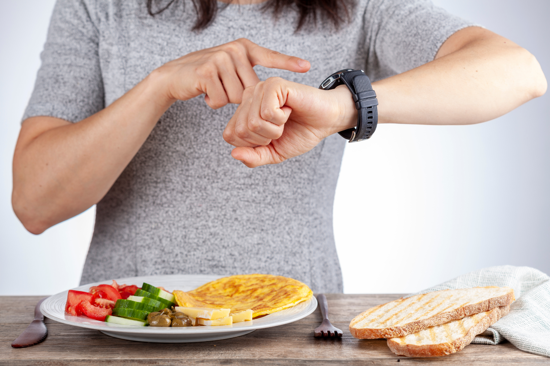 women looking at her watch, with breakfast plate in front of her. Checking her fasting schedule