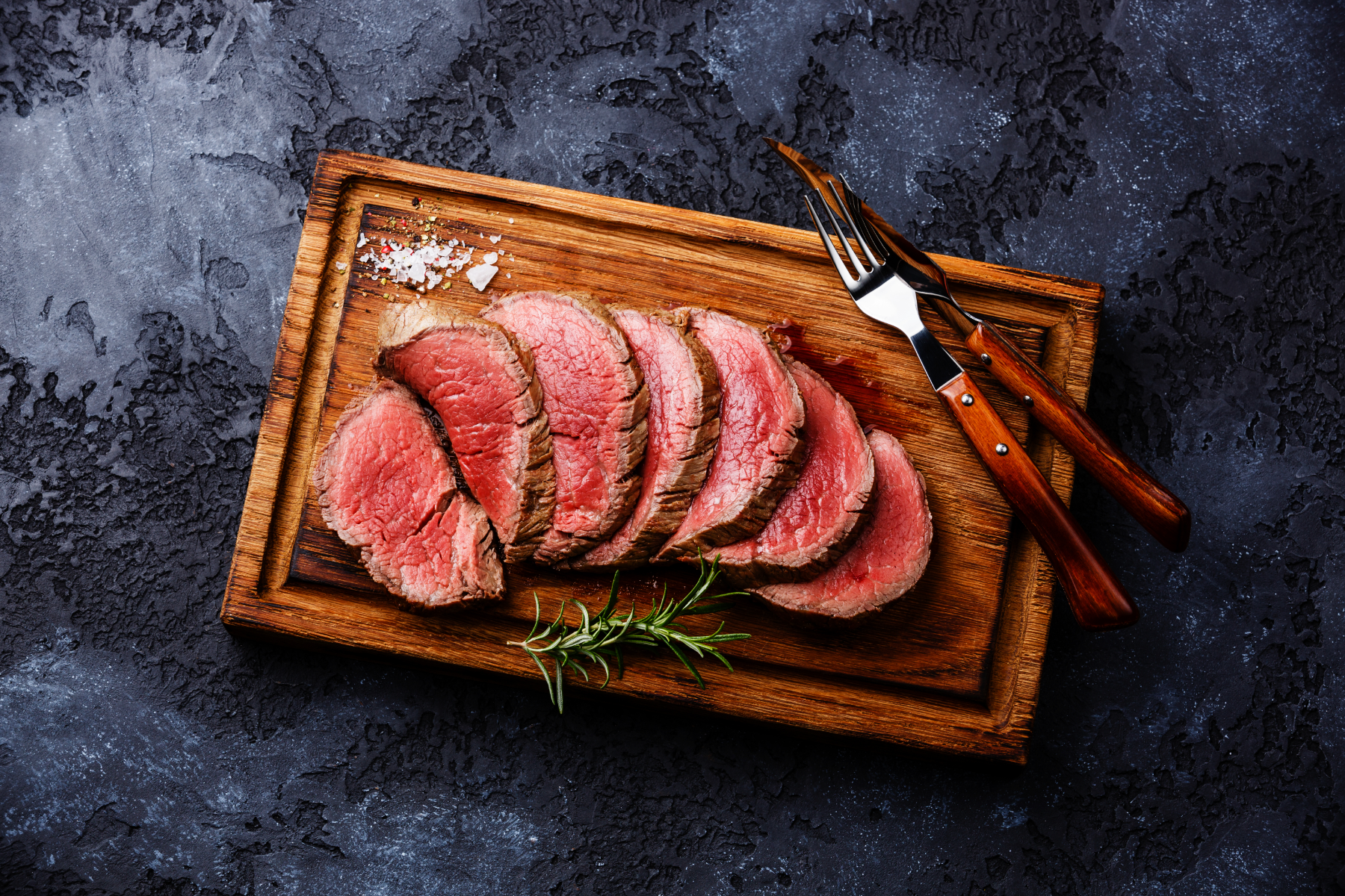 Sliced steak on a cutting board with fork and steak knife