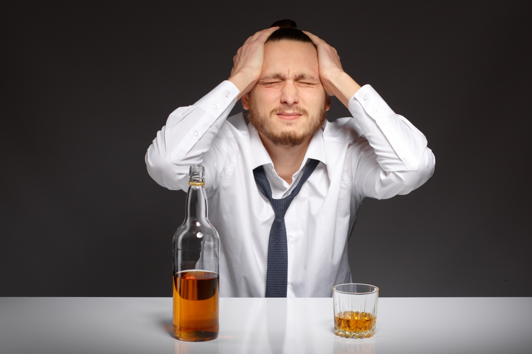 man grabbing his head in frustration with a bottle of whisky in front of him