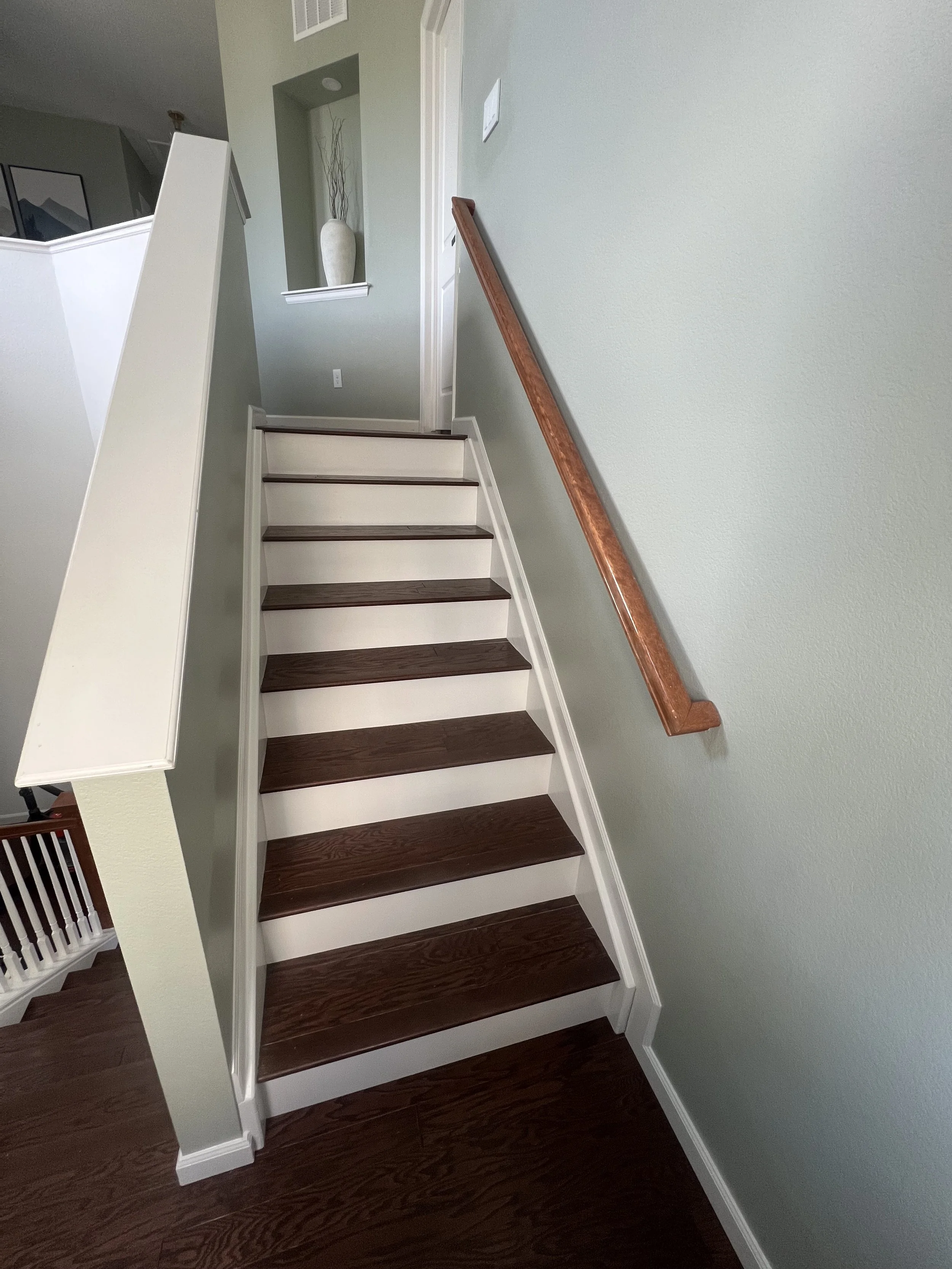 Indoor staircase with dark wooden steps and a matching handrail on a green wall.