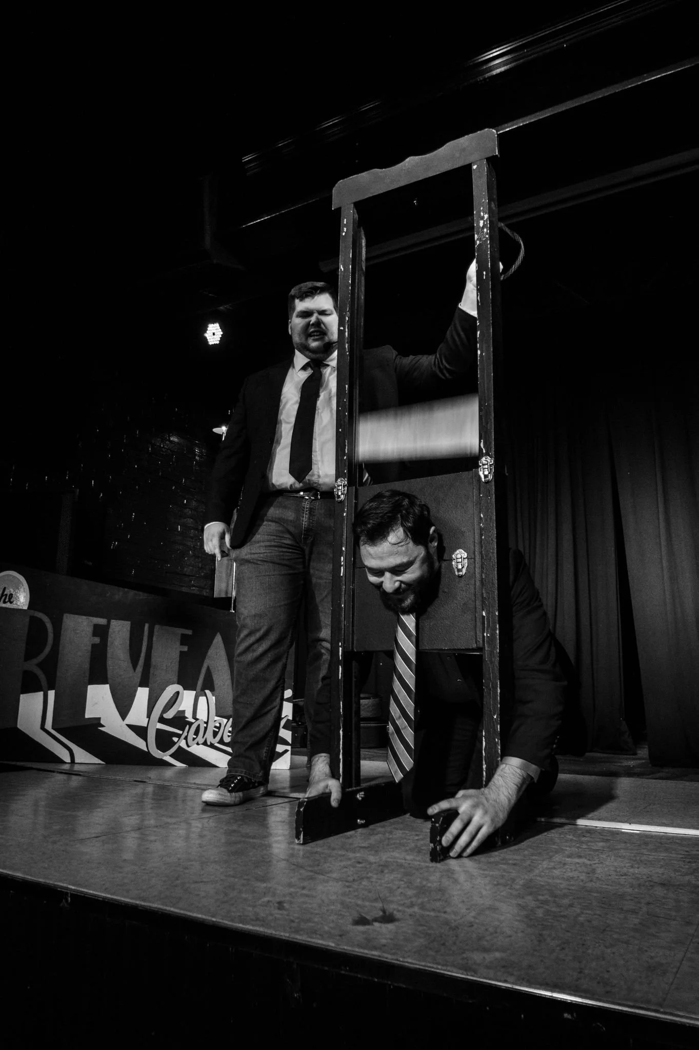 Two men in formal attire perform an illusion or magic act on stage involving a large frame and a box. Corporate Magician Seth Dreams stands with his eyes closed and an intense expression, while the other man is inside the box, looking down.
