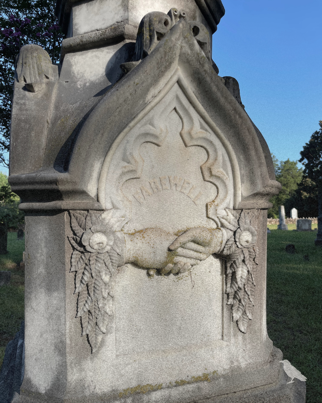 Historic cemetery monument featuring carved clasped hands, floral details, and weathered stone.