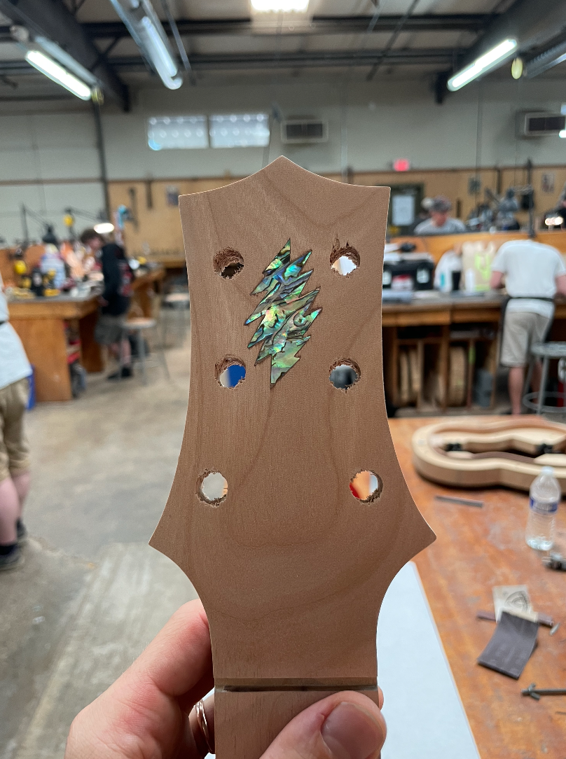 Close-up of a guitar headstock with a lightning bolt-shaped inlay in abalone shell, at Lineage Guitars workshop in San Francisco.