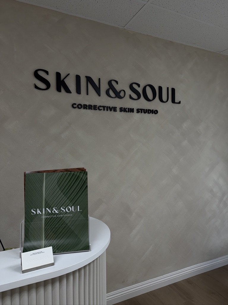 Interior of a skincare studio with the sign 'SKIN & SOUL' and 'Corrective Skin Studio' on the wall; a table holding promotional materials for the studio.
