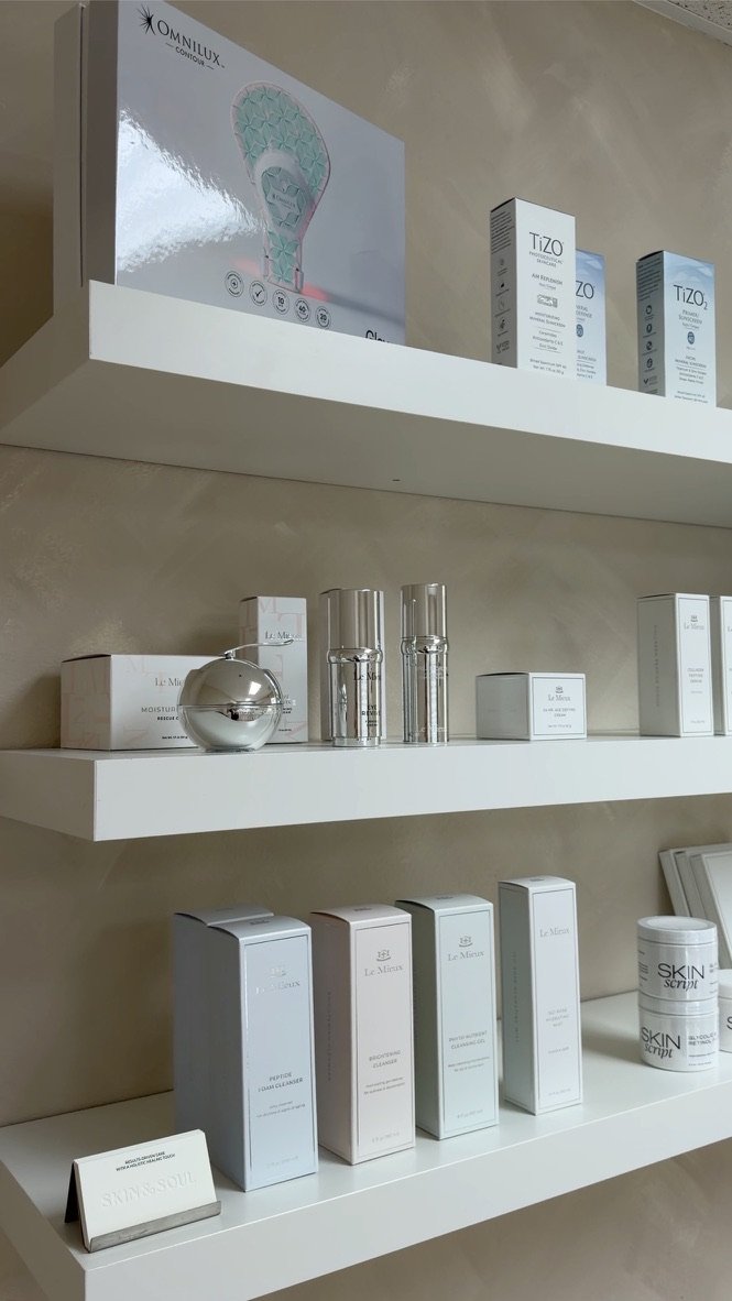 Display of skincare and cosmetic products on white shelves, including boxes labeled Le Mieux and Skin Script, and various bottles and containers, in a retail or clinic setting.