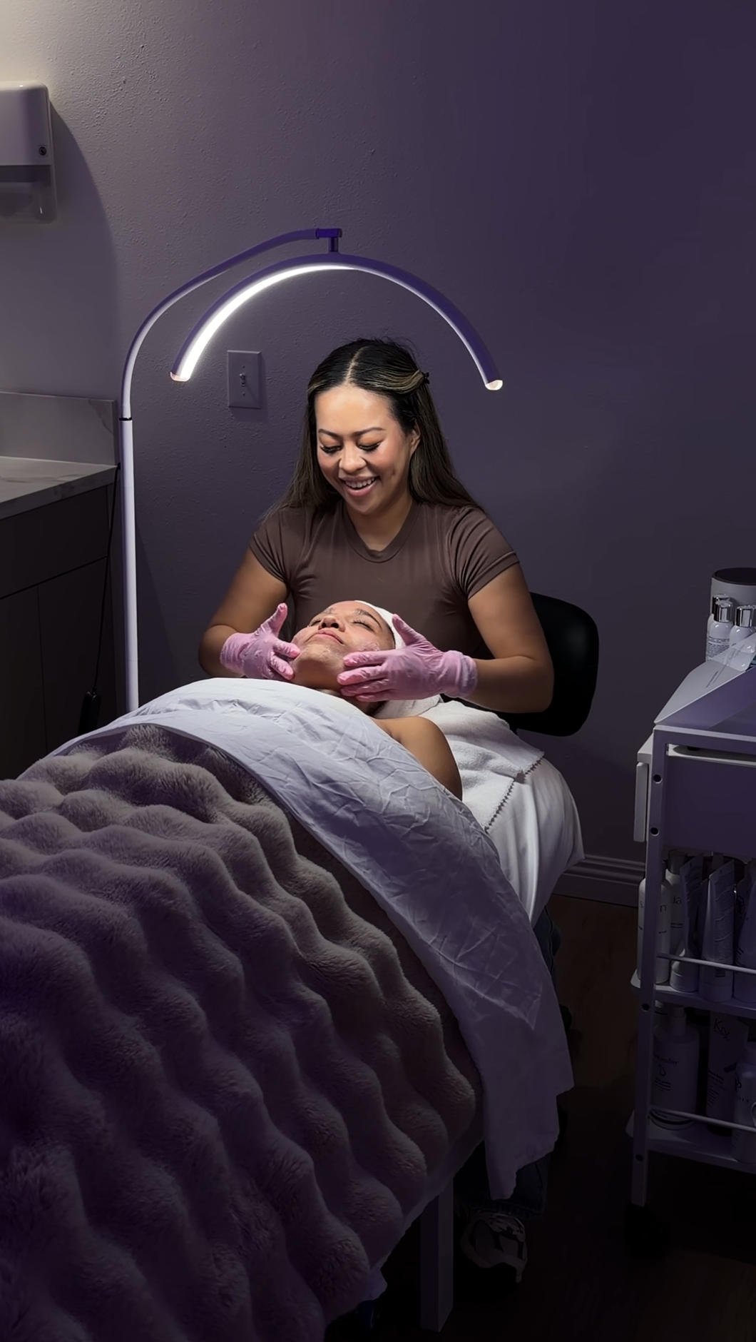 A woman is getting a facial consultation from a professional wearing gloves in the treatment room
