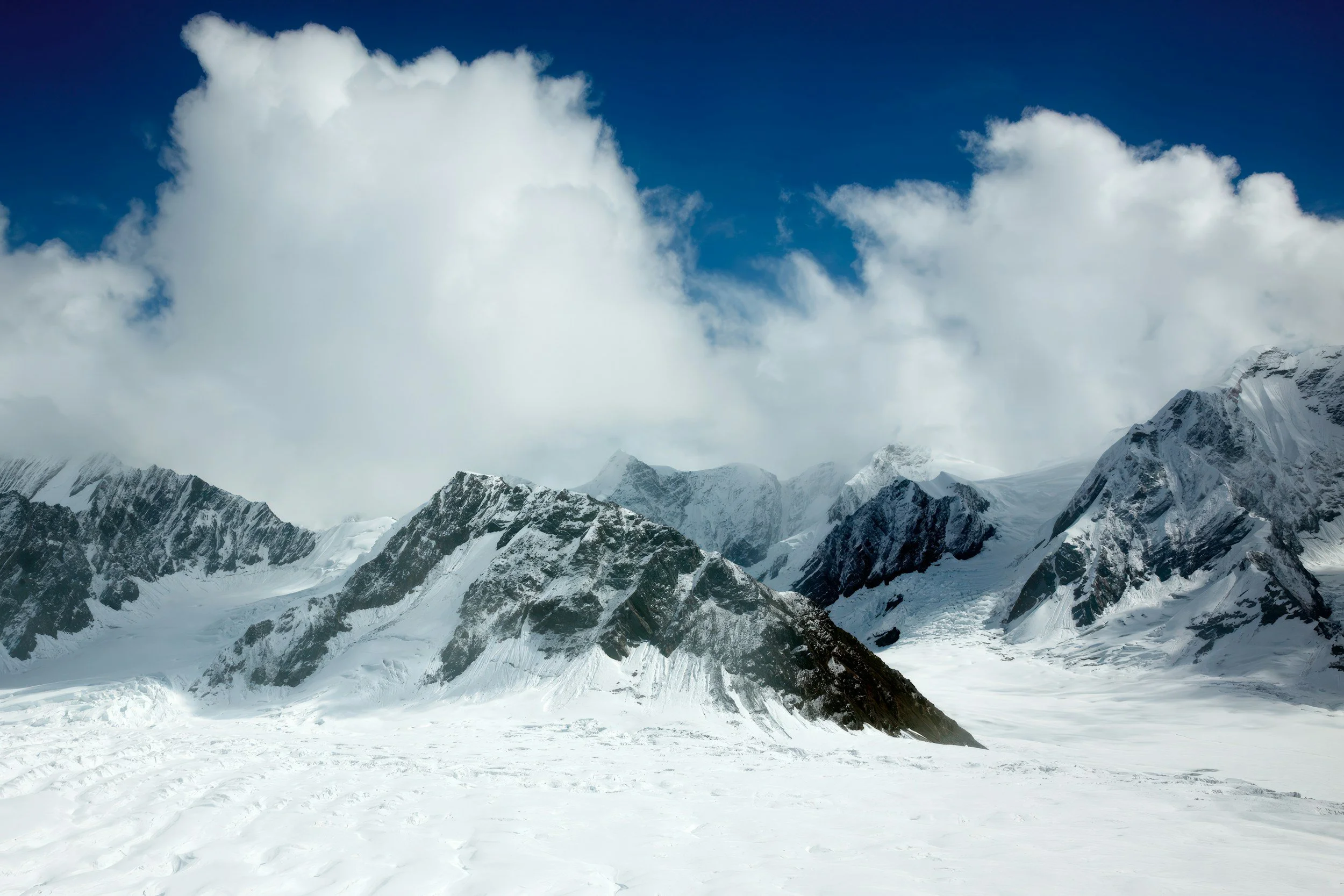 Scenic mountain landscape with snow-capped peaks, green rolling hills, and a winding river in the valley.