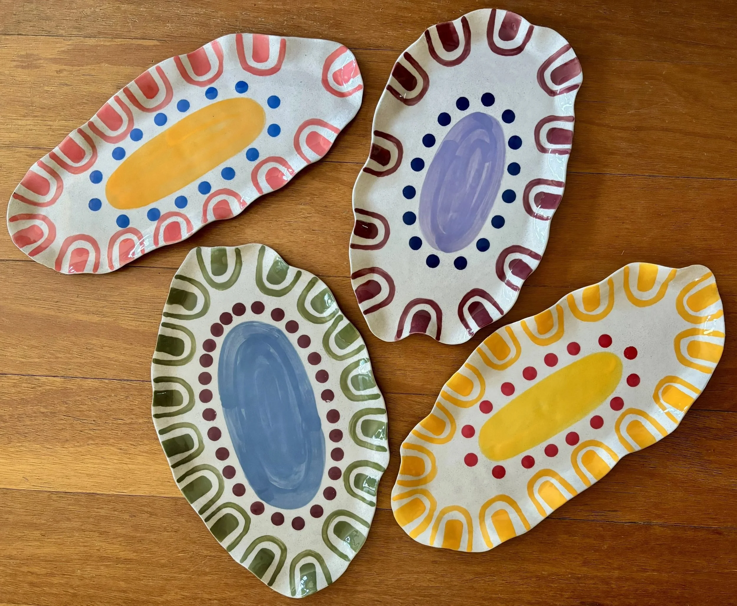 Four decorative oval ceramic plates with colorful patterns placed on a wooden surface.