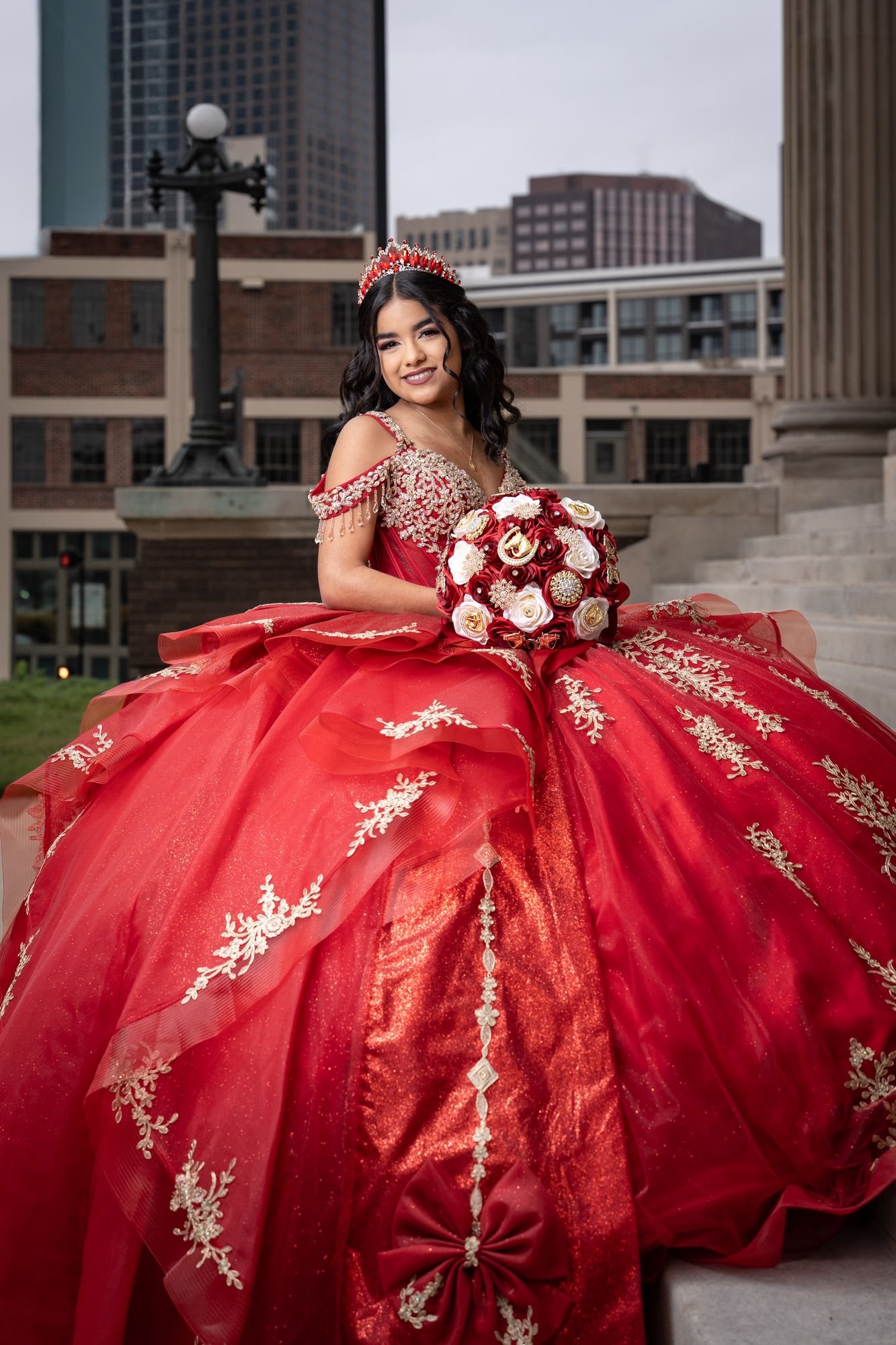 Red quinceañera gown at the Scottish Rite Cathedral with Dallas downtown skyline, full-length front view showing the gold-embroidered bodice and layered tulle skirt