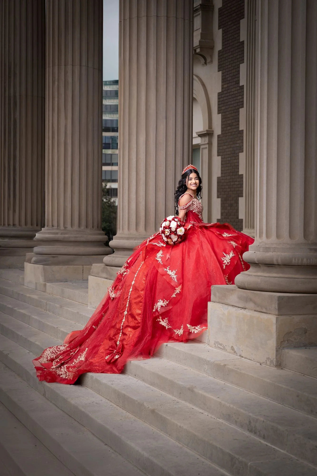 Red quinceañera dress rental from Rafaela's, seated portrait on the Scottish Rite Cathedral steps between stone columns in downtown Dallas