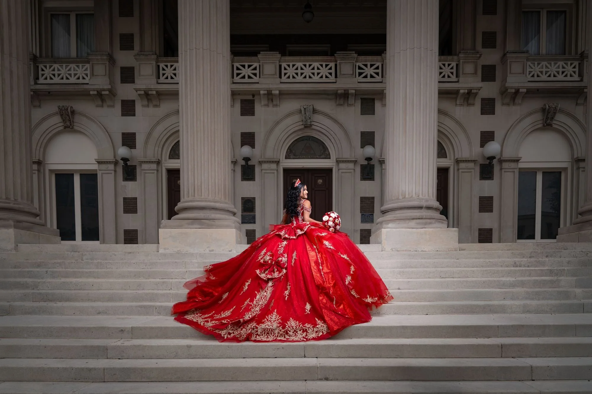 Red quinceañera ballgown train spread across the steps of the Scottish Rite Cathedral in downtown Dallas, showing the gold embroidered hem and silhouette