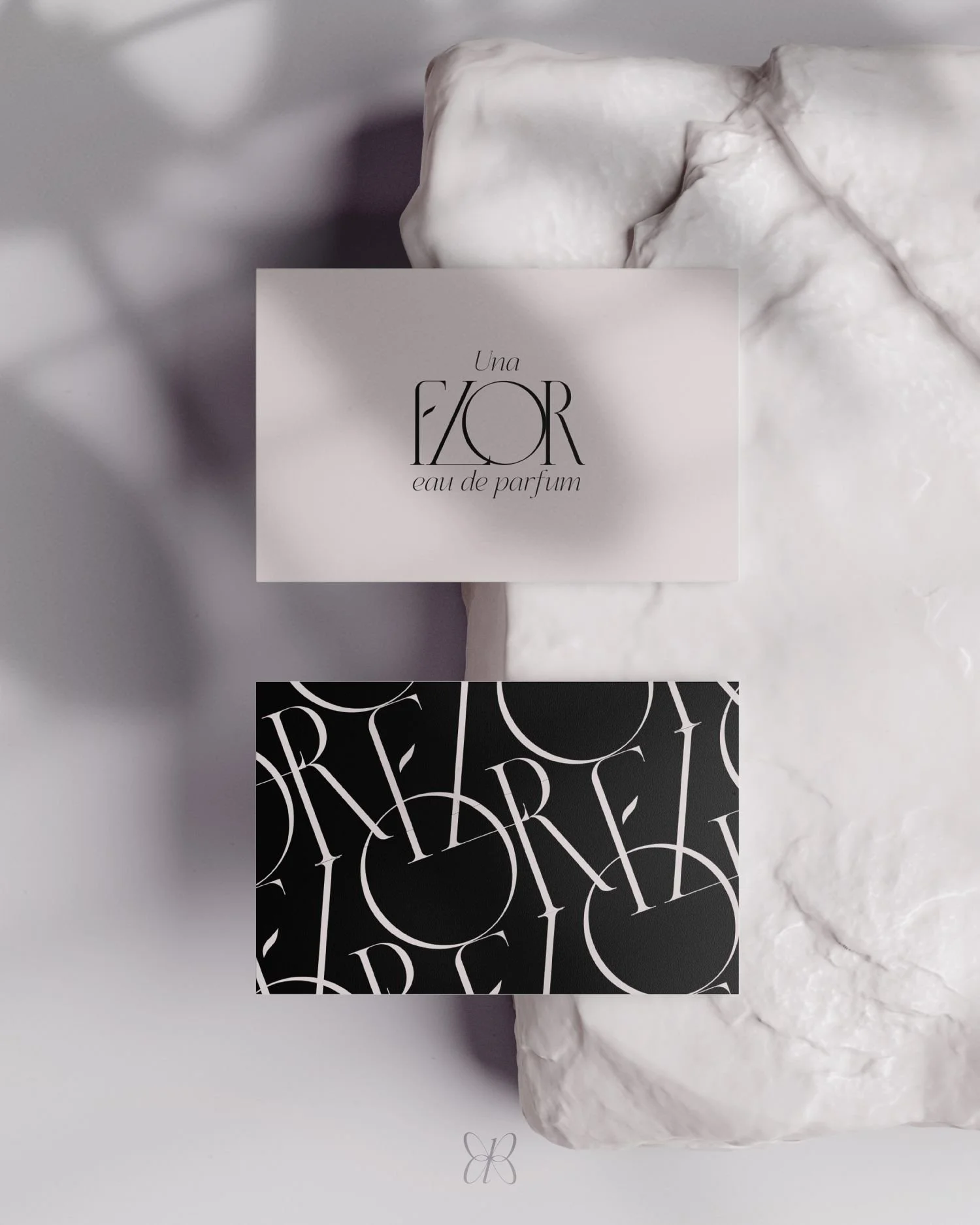 Close-up of two perfume labels resting on white textured stones. The top label is light pink with black text reading 'Una Flor eau de parfum.' The bottom label is black with white stylized text.