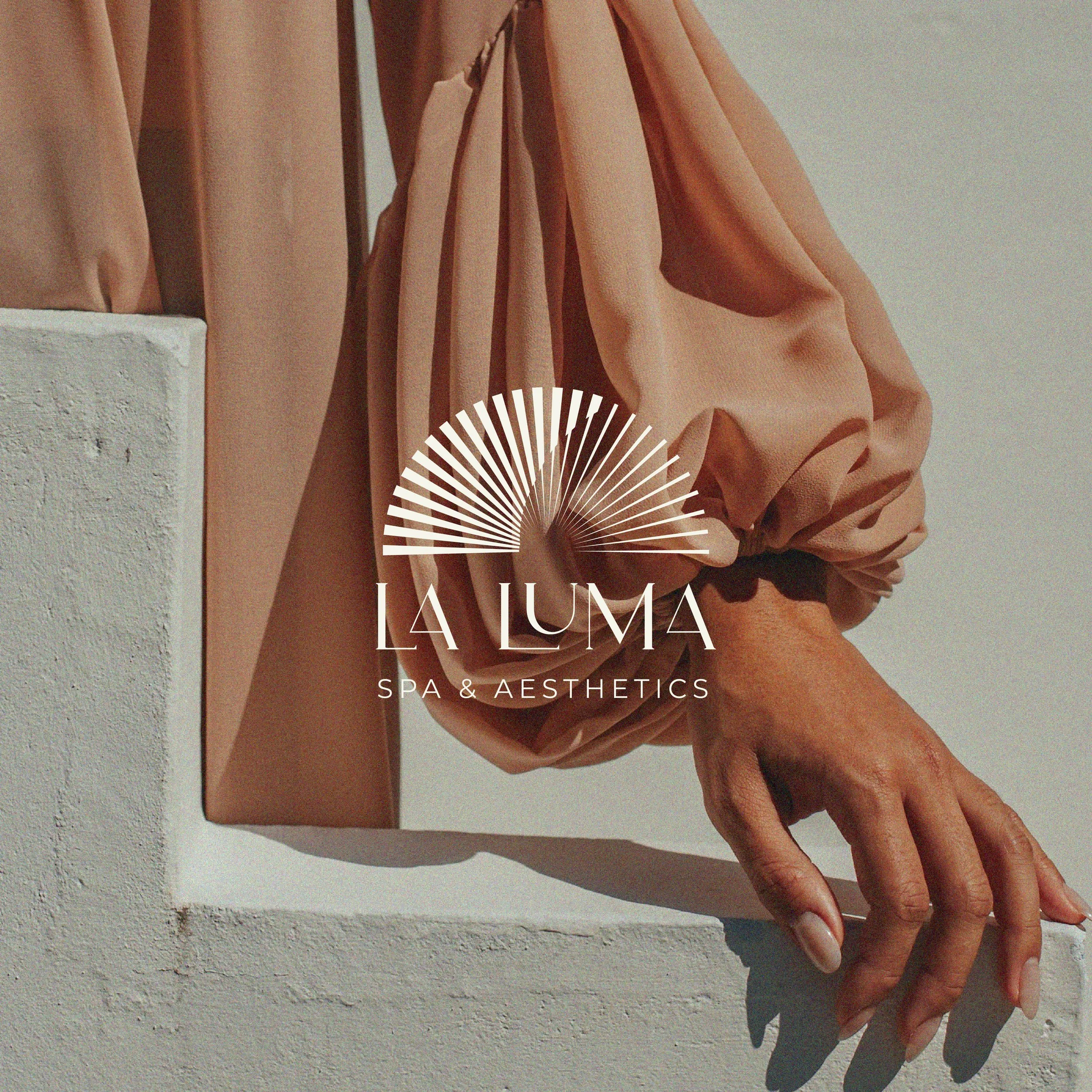 Logo for La Luma Spa & Aesthetics over a background of a hand resting on a white surface, with a beige long-sleeve garment draped over the arm.