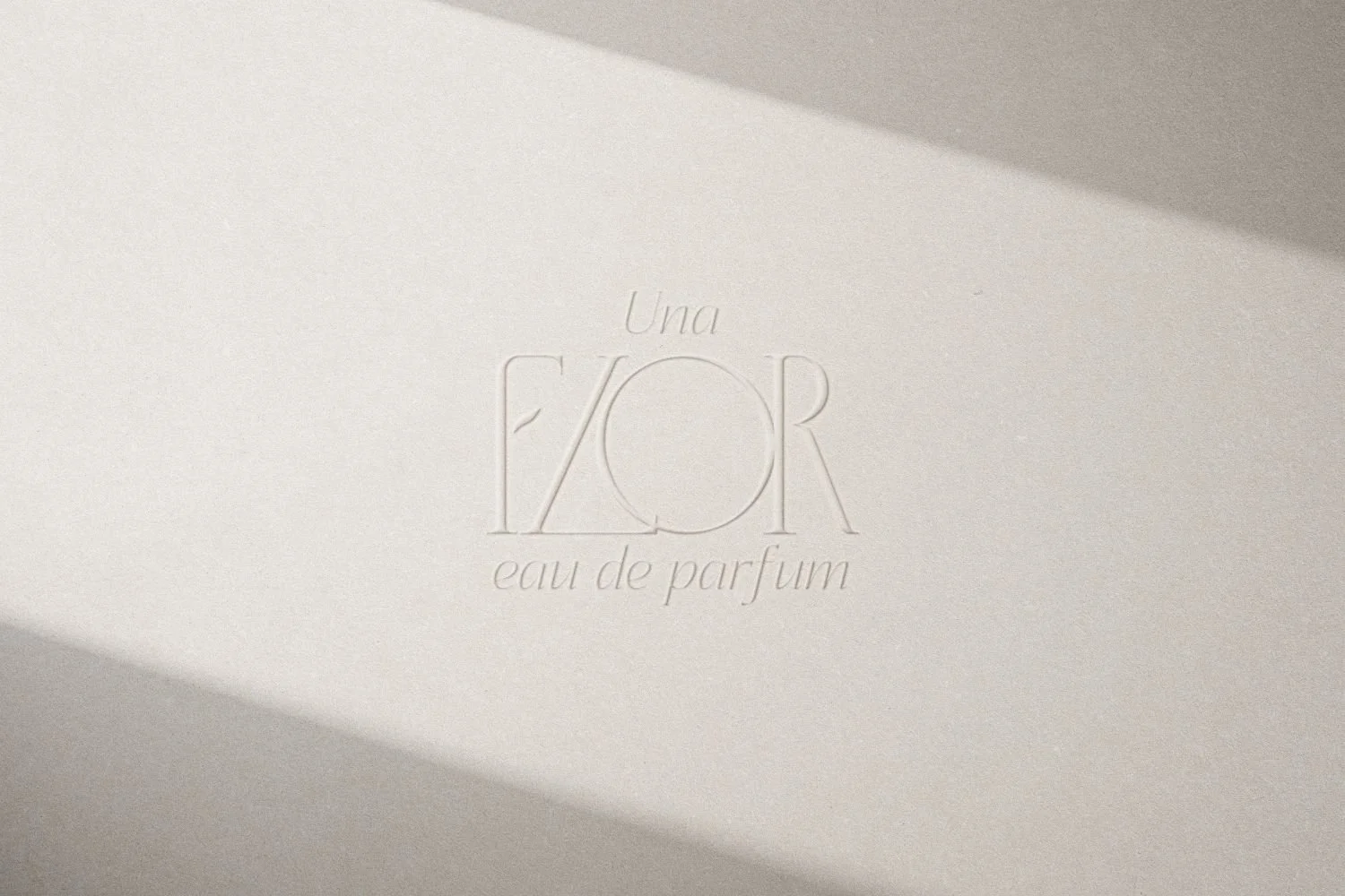 Light-colored textured surface with embossed text reading "Una FIOR eau de parfum" and a shadow cast across the top right corner.
