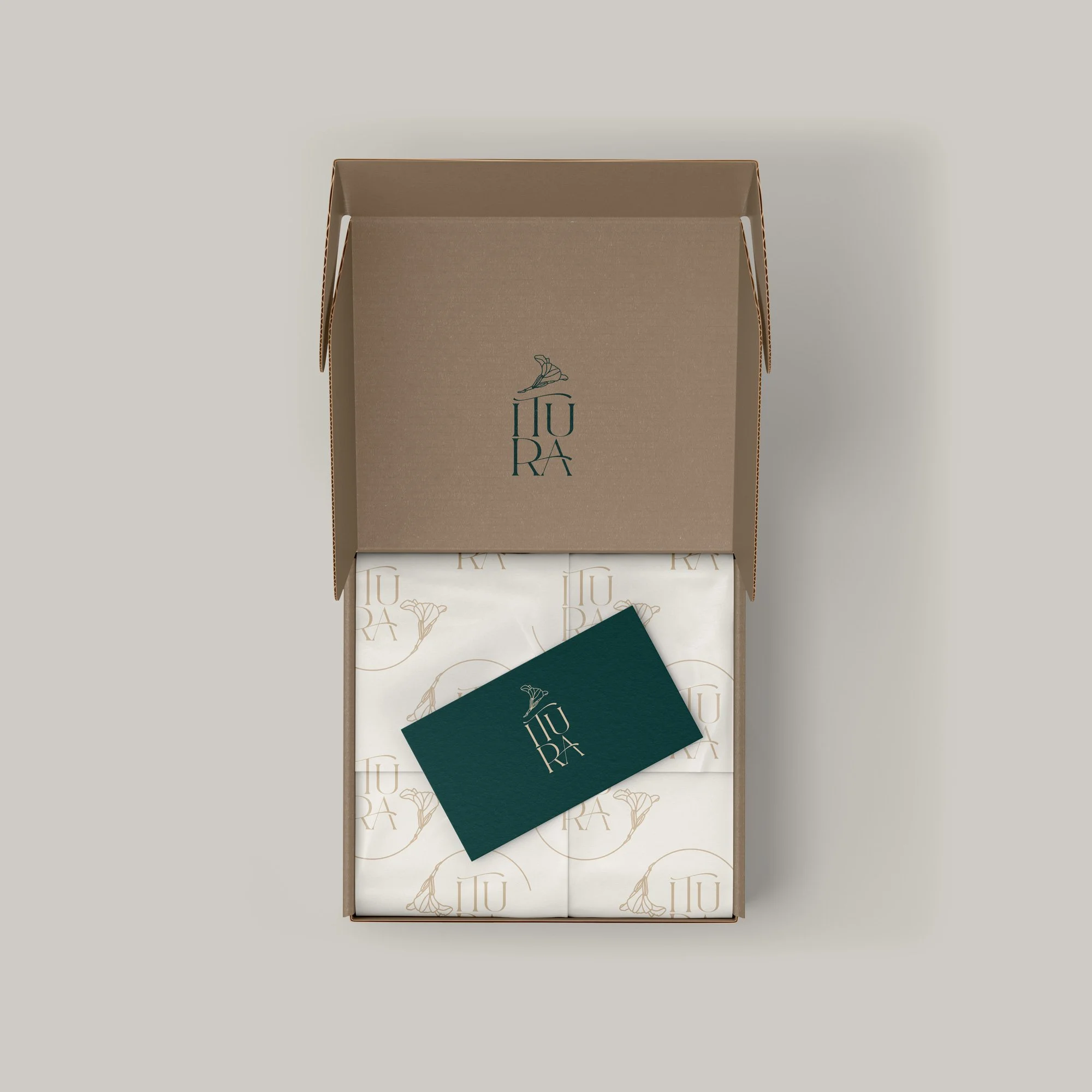 Open cardboard box containing wrapped products and a card with a logo for 'IUUR'. The logo features a stylized flower with text underneath.