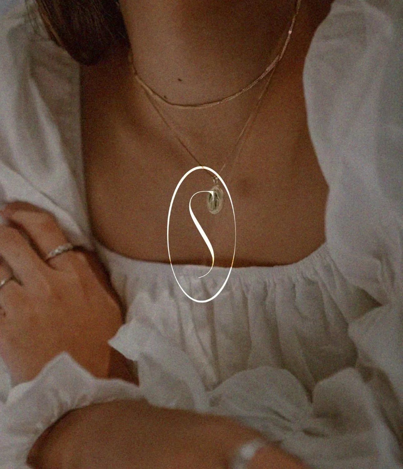 A person wearing jewelry, with necklaces and rings, partly covered by a white garment, lying down or reclining.