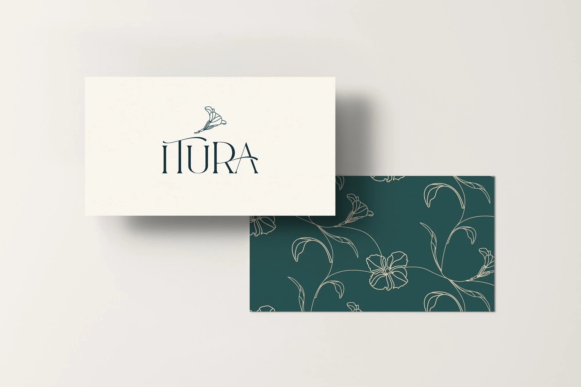 A white card with the word 'IIURA' and a butterfly illustration on top, placed over a dark green card with a floral line art pattern.