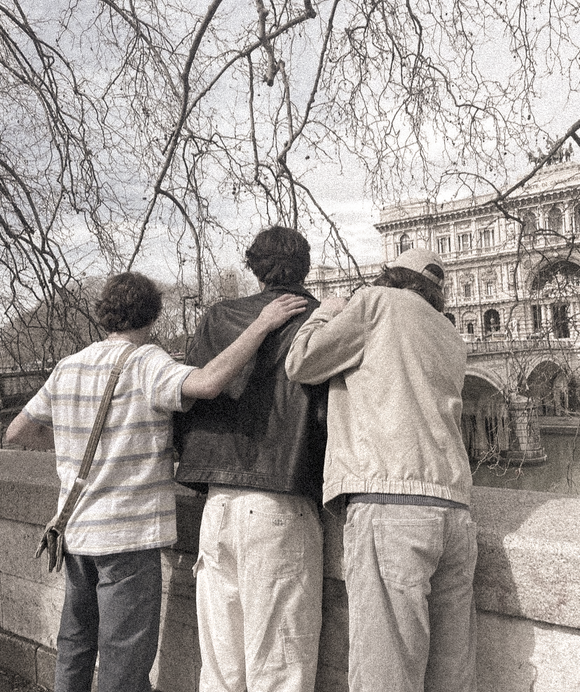 three boys stand at a fence railing looking at a large white building
