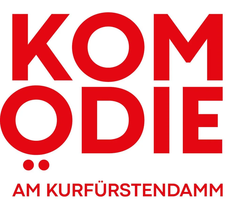 Das Bild zeigt einen roten Schriftzug, der „KOMÖDIE“ mit zwei Punkten und darunter in kleinerer Schrift „AM KURFÜRSTENDAMM“ auf weißem Hintergrund buchstabiert.