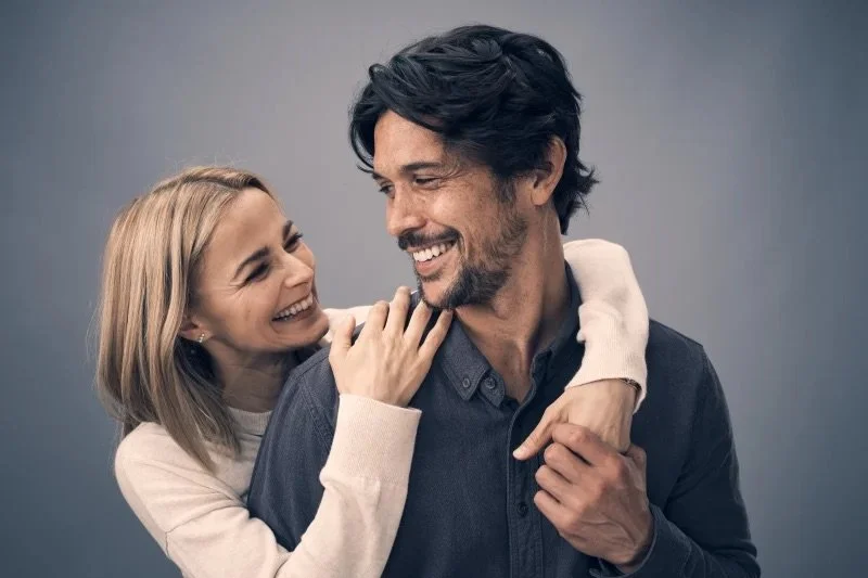 A woman and man smiling and embracing against a neutral background.