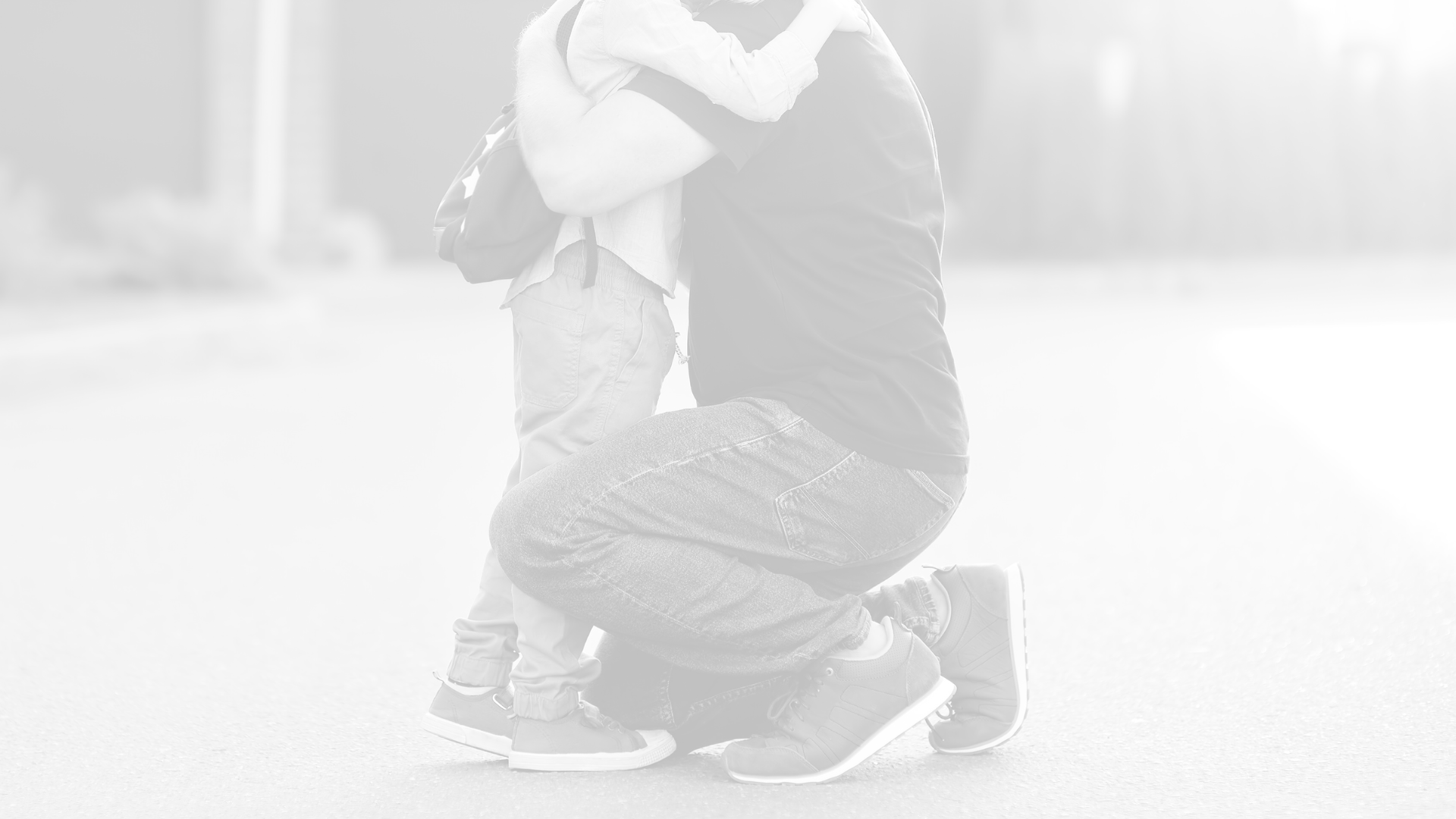 A child and adult hugging outdoors on a sunny day.