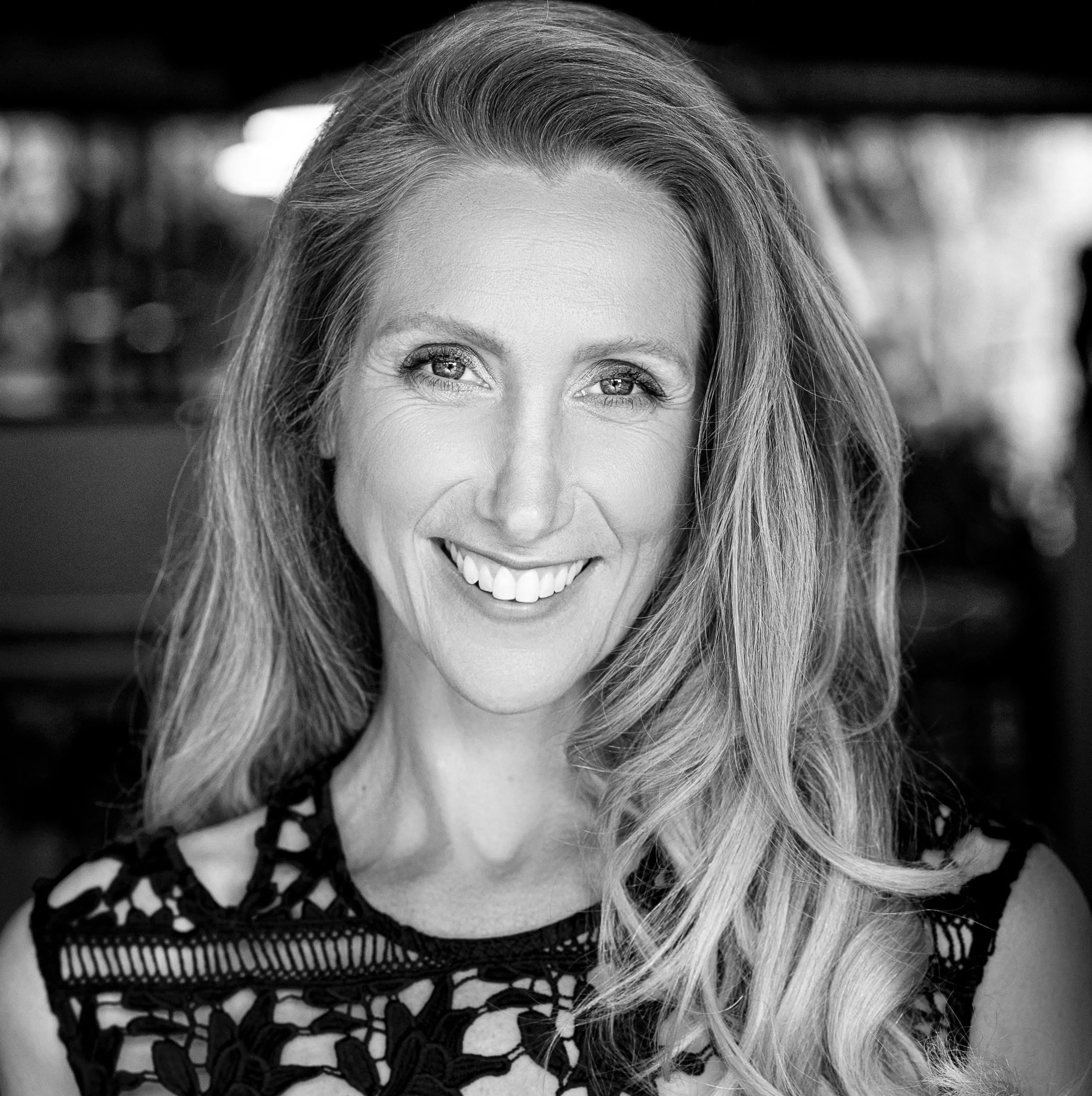 Black and white portrait of a woman with long wavy hair, smiling, wearing a lace top.