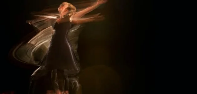 A person dancing on a dark stage with motion blur effects.