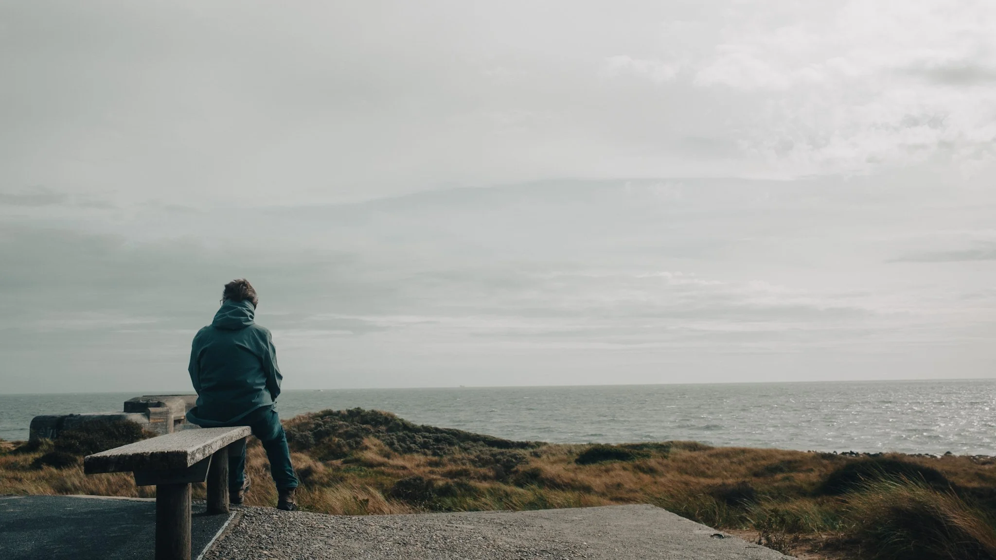 Man sitting on a bench overlooking the ocean on a cloudy day.
