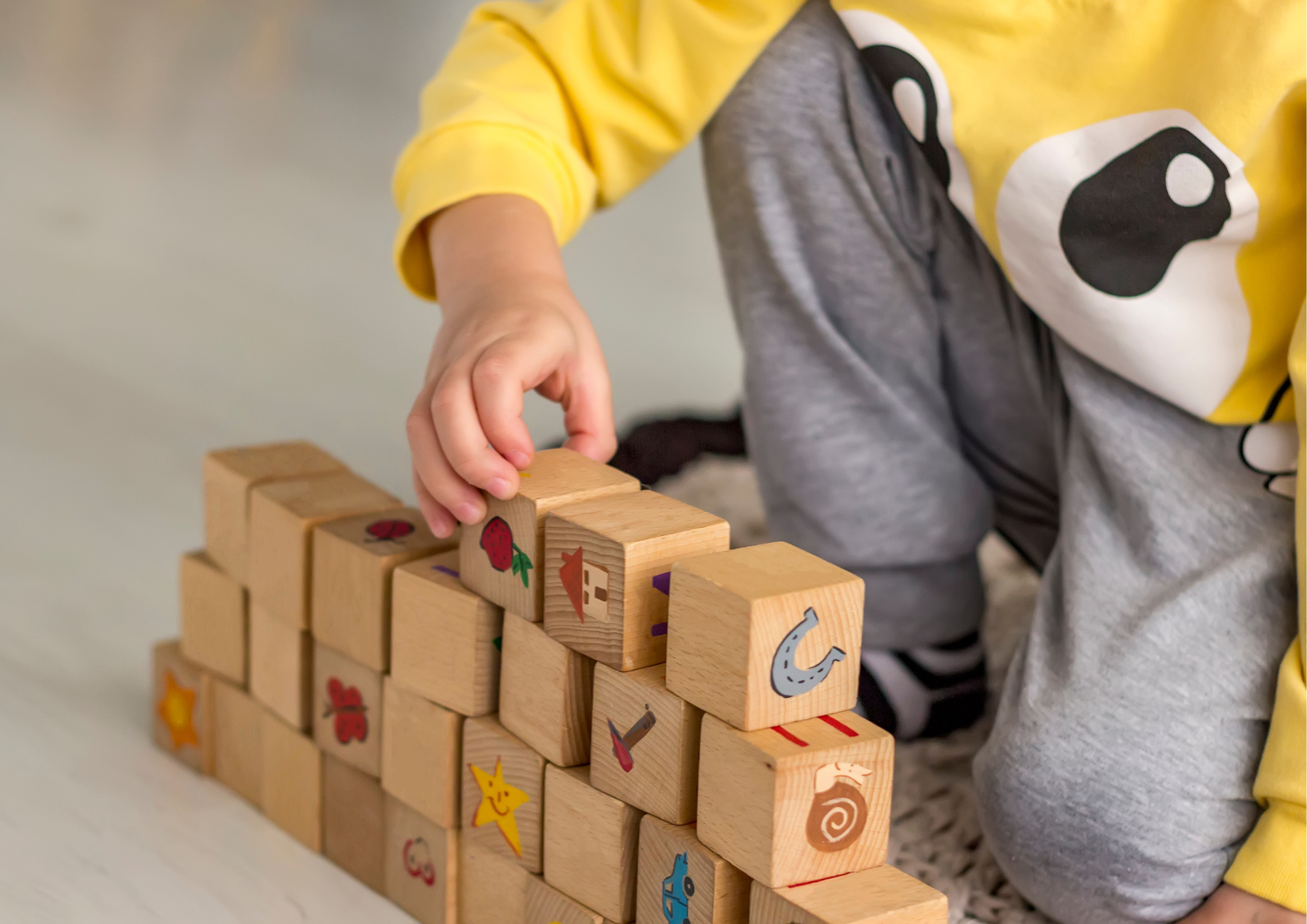 Child playing with wooden blocks, wearing a yellow and grey outfit