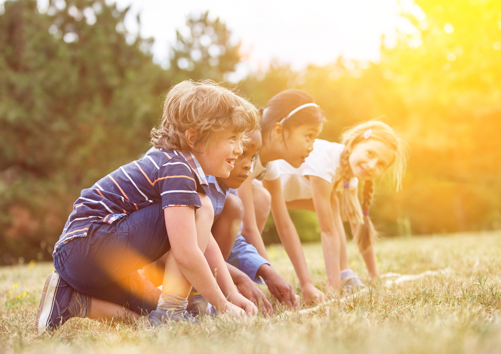 Children crouching in a field, preparing to run; sunny outdoor setting.
