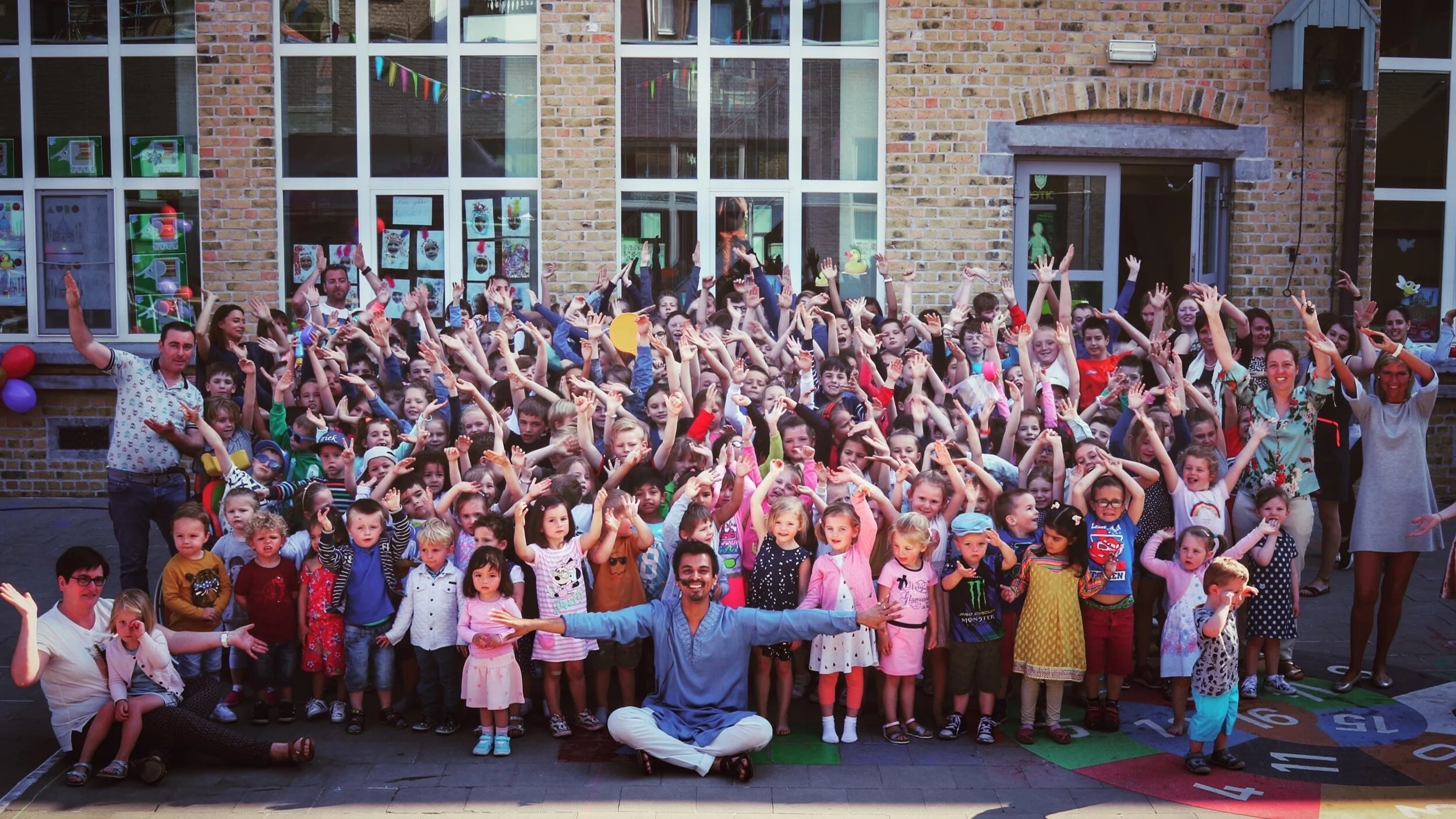 Group of children and adults celebrating with raised arms outside a brick building.