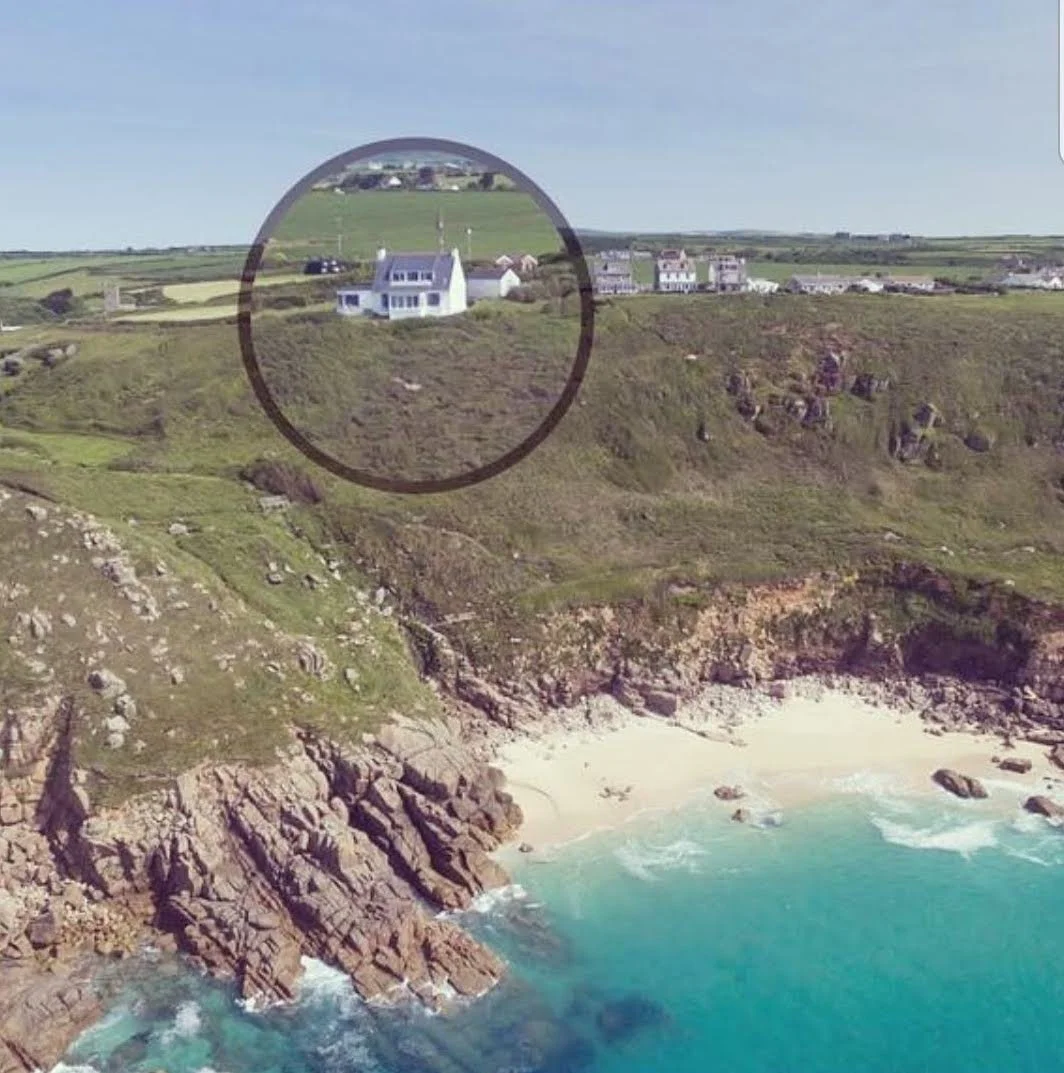 A coastal landscape with rocky cliffs and a beach, and houses on the grassy hilltop. A circular overlay highlights a house on the hill.
