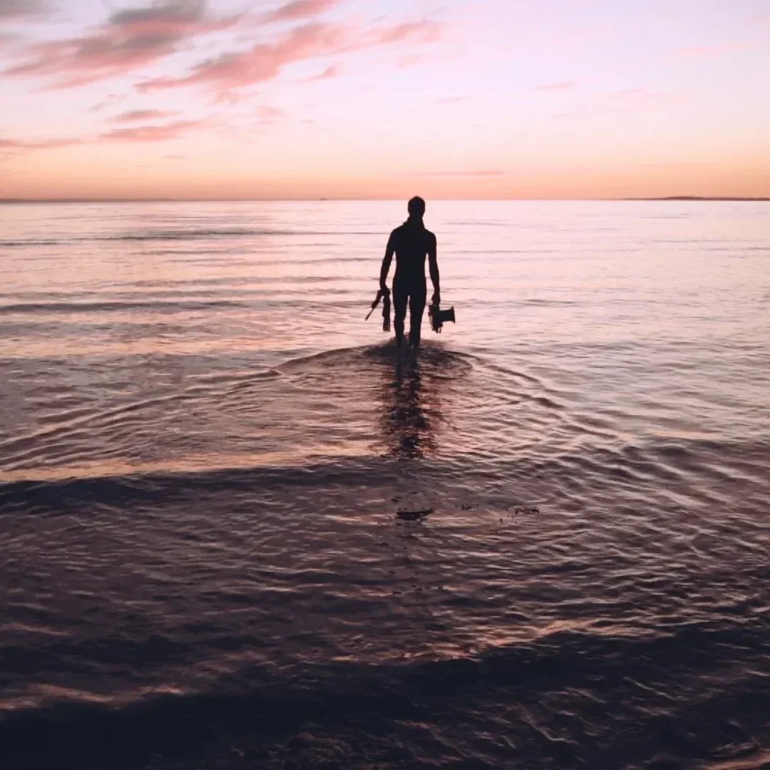 A man walks into the sea with diving gear in the morning pre sunrise dawn